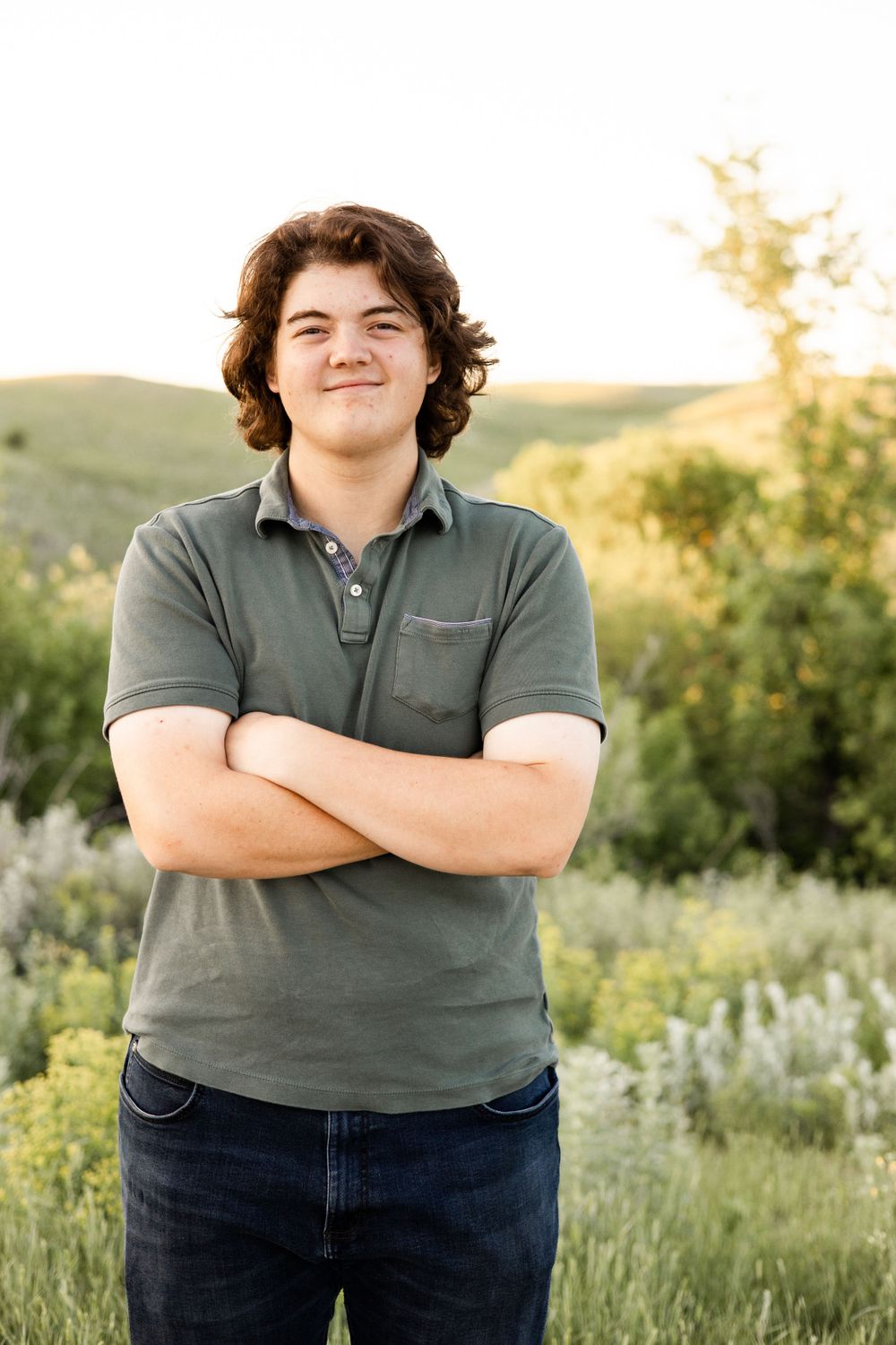 Young person in grey polo shirt standing outdoors in natural setting at sunset.