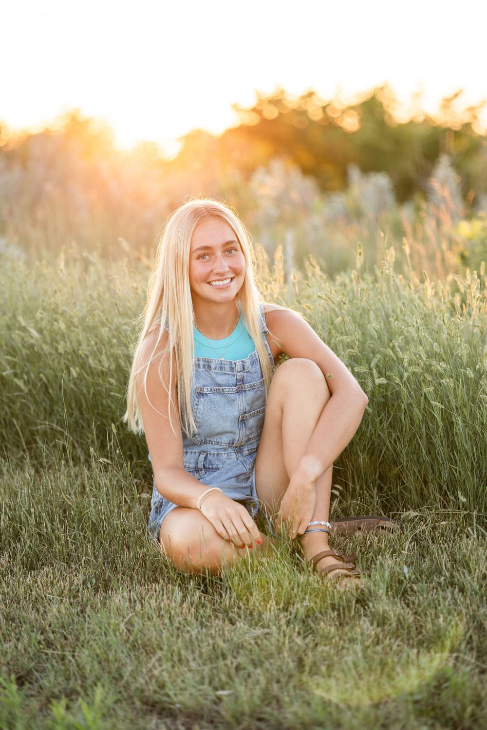 Person in overalls sitting in wildflower field at sunset.