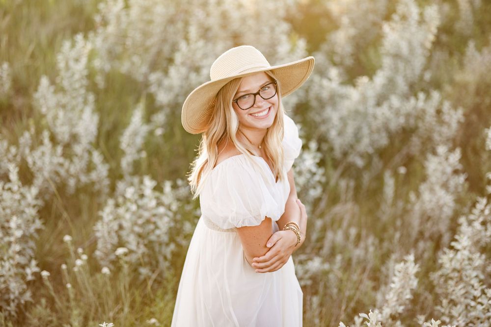 Person in white dress and straw hat standing in golden field at sunset.