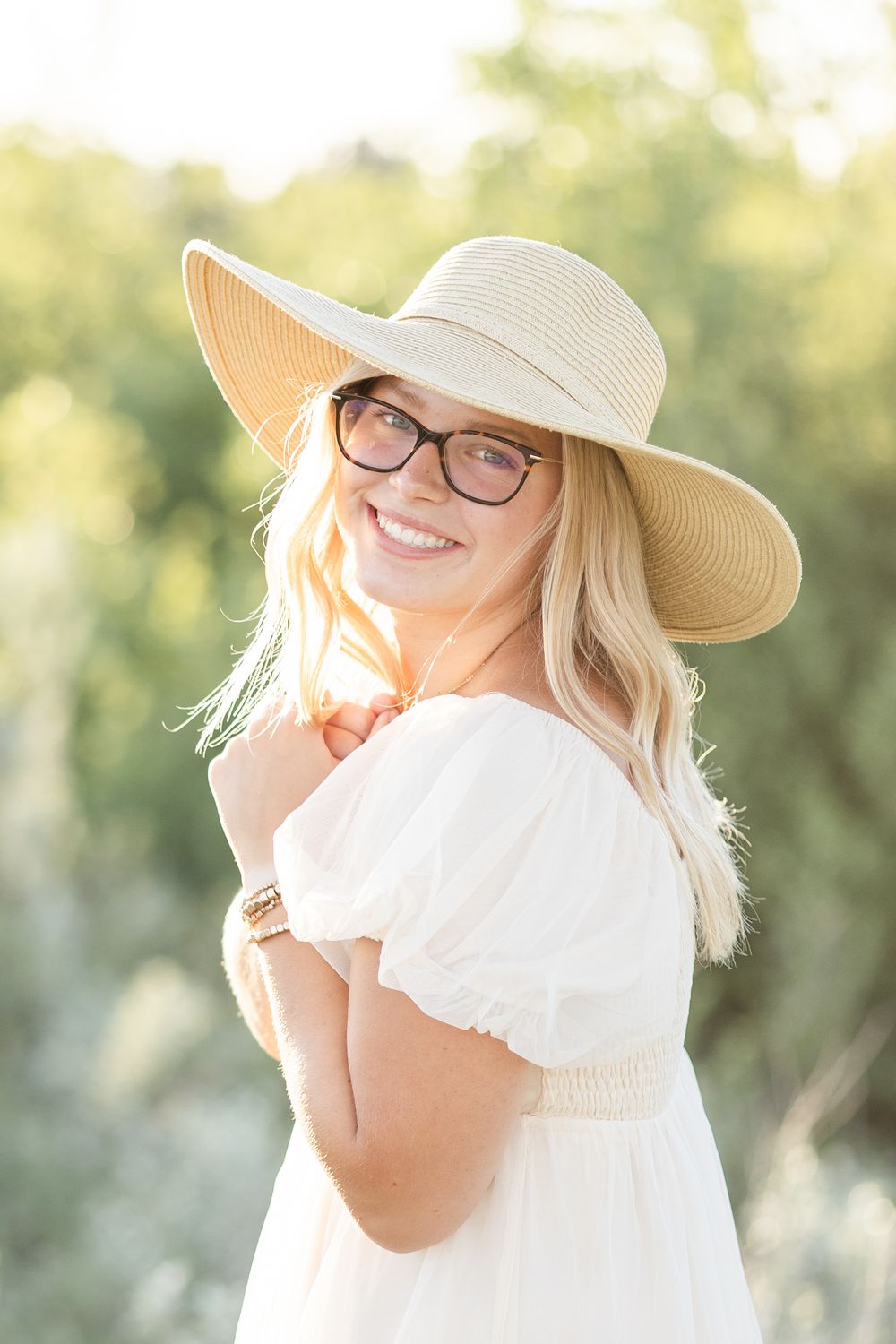 Person in white dress and sun hat posing in warm summer lighting.