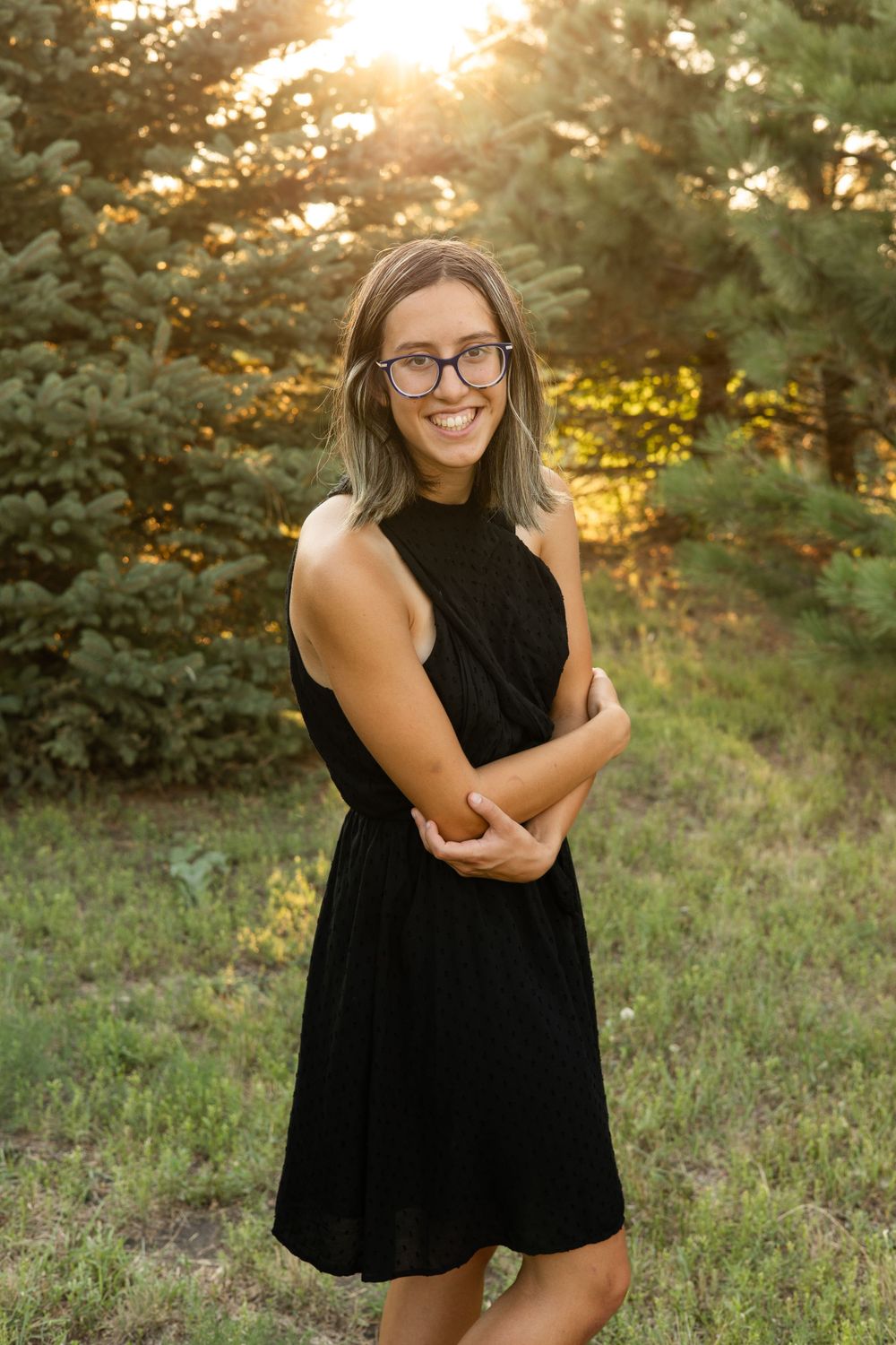 Person in black halter dress posing against sunset forest backdrop.