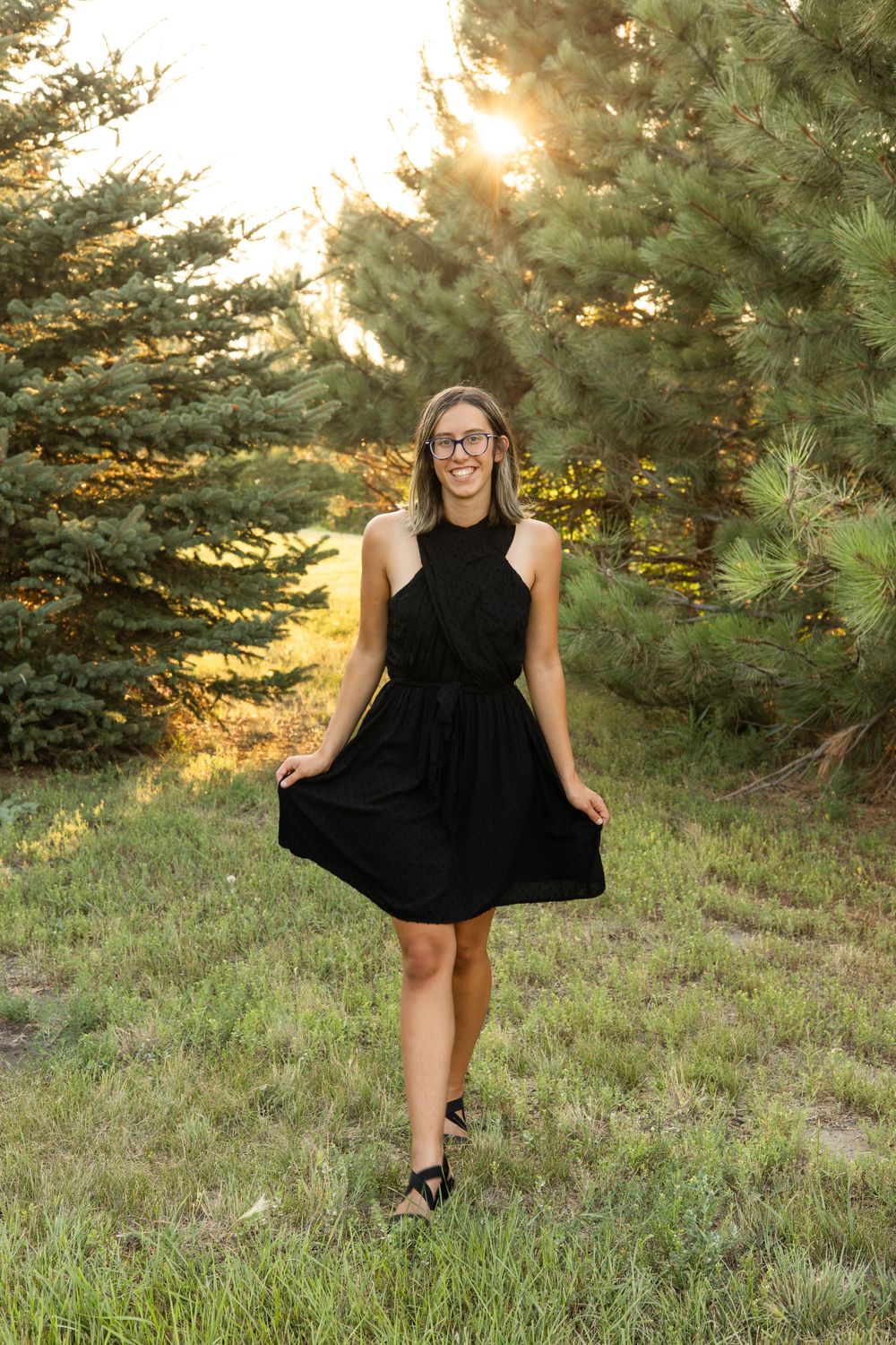Person in black dress twirling in sunset-lit forest setting.