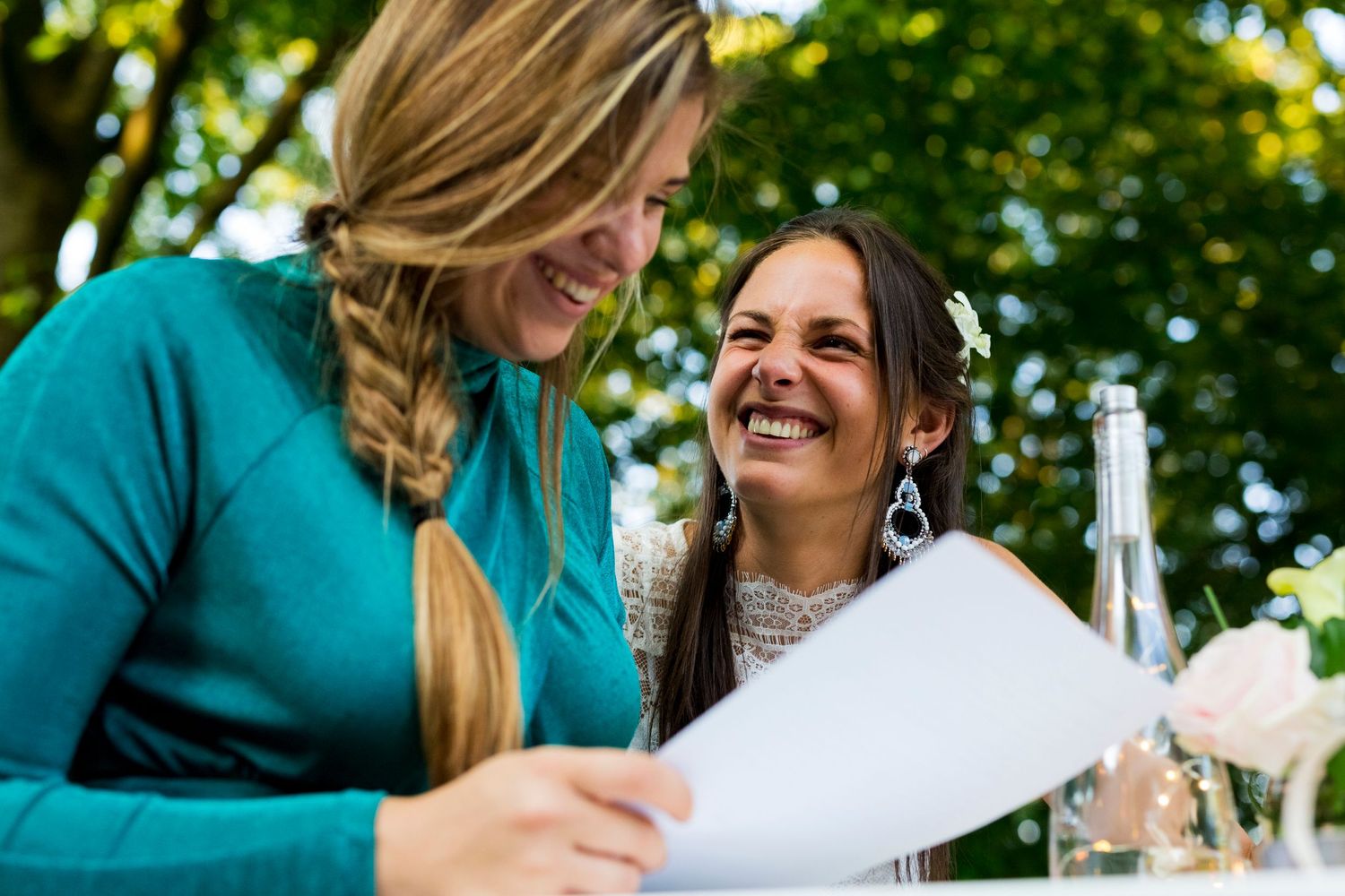Two people sharing laughter while looking at documents during an outdoor gathering.