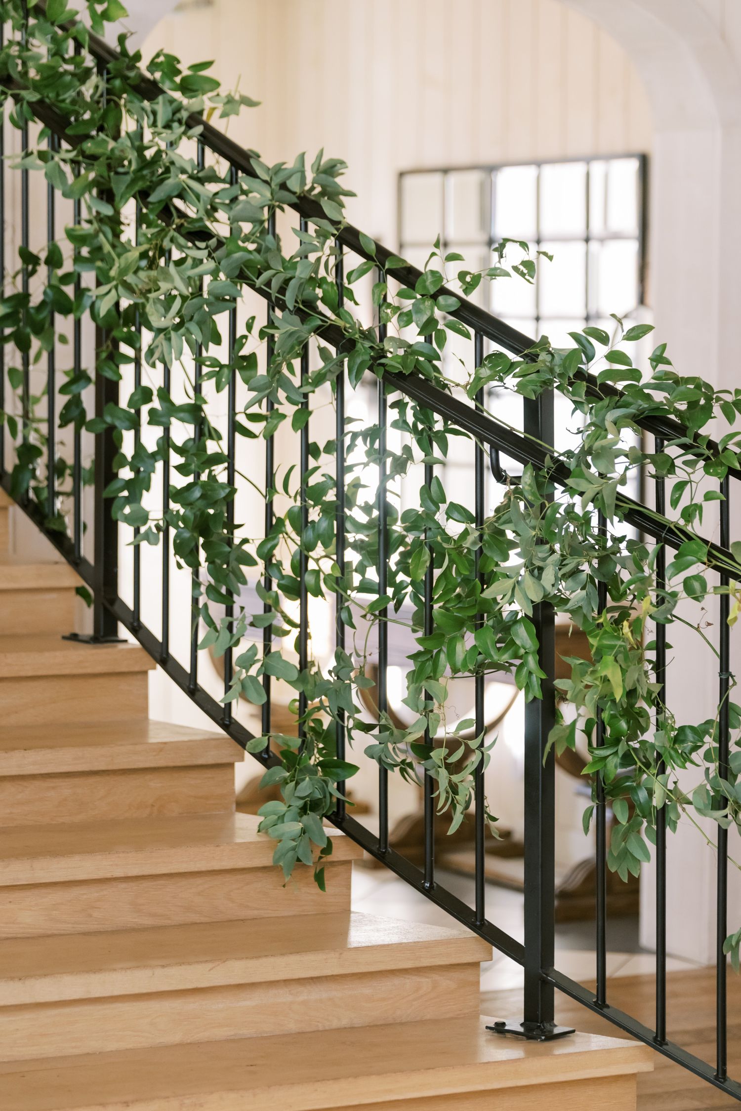 Elegant staircase with lush greenery garland winding along black metal railing.