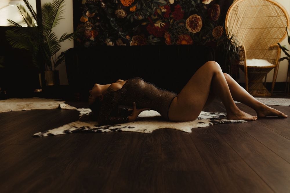 Artistic boudoir photo with moody lighting on hardwood floor featuring dramatic shadows.