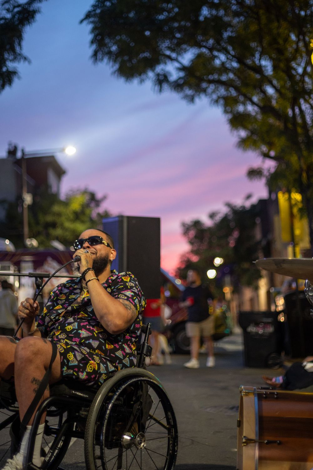 A performer in a wheelchair sings at an outdoor concert during sunset.