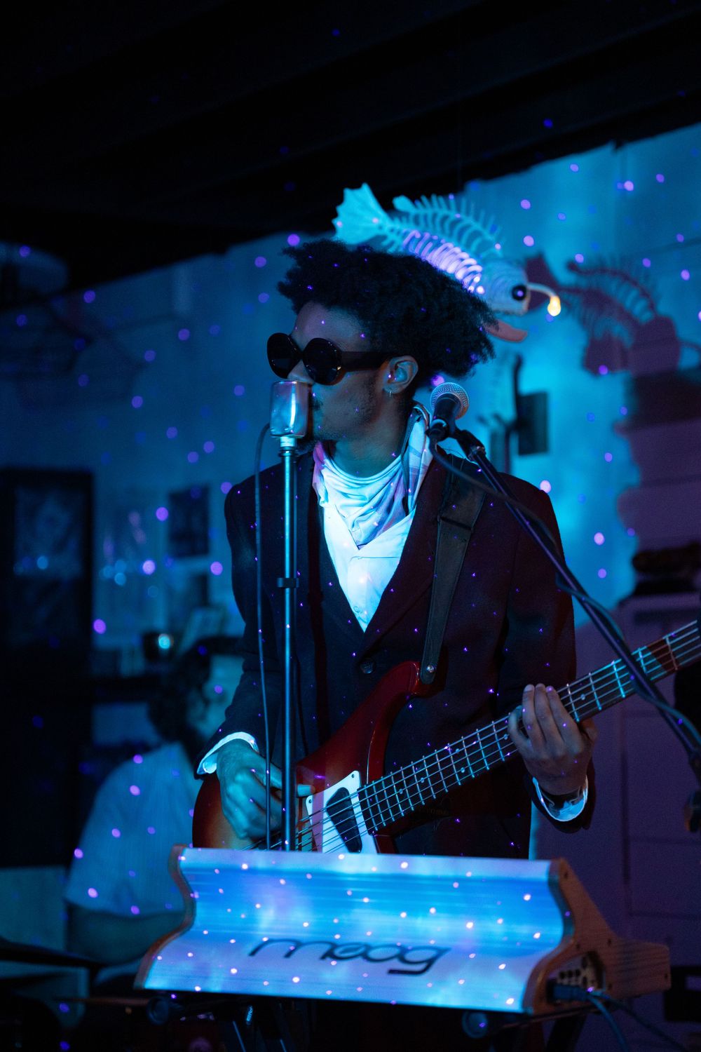 Musician performing with a bass guitar under dramatic blue lighting at a nightclub venue.