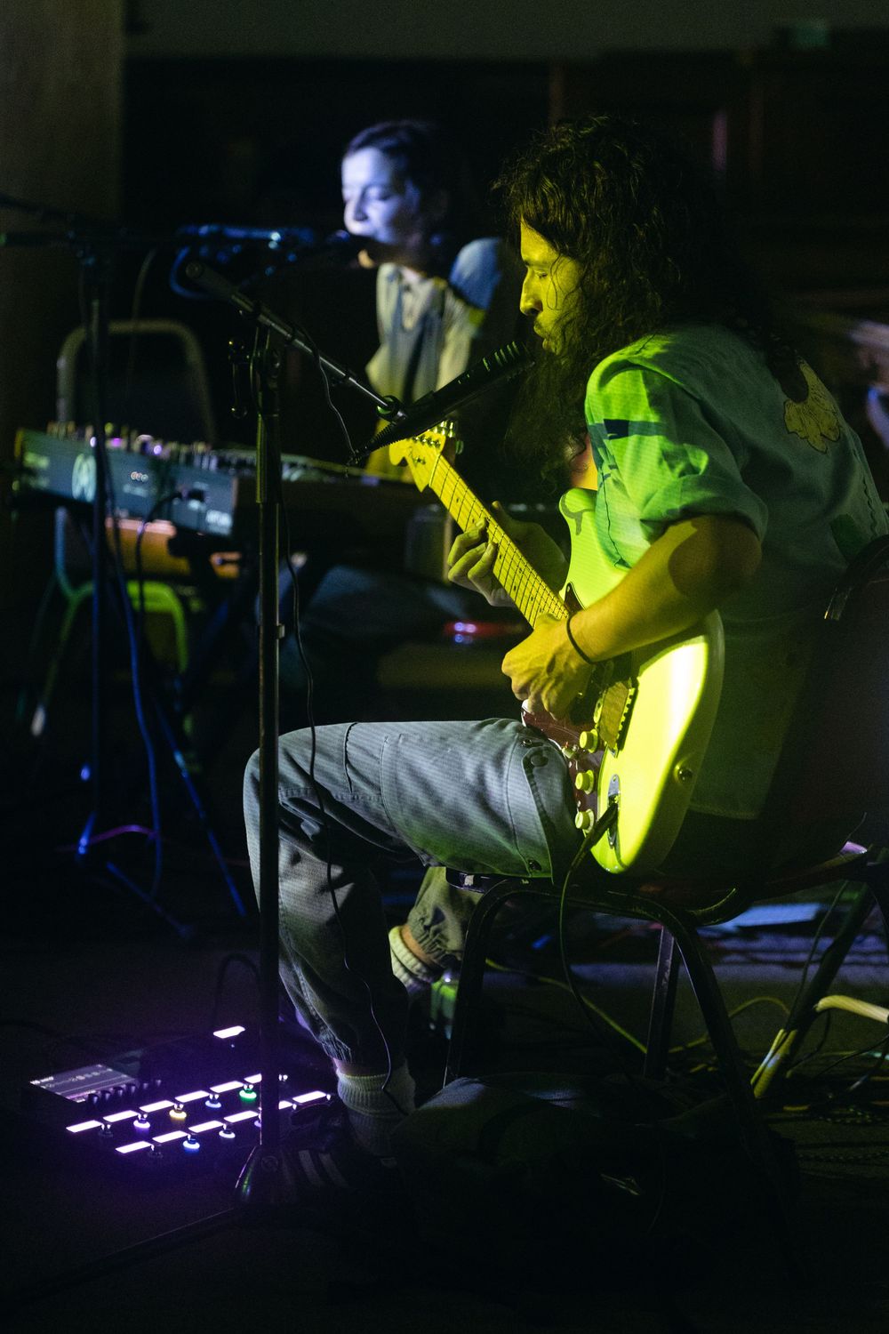 A guitarist performs under dramatic yellow stage lighting in a dark concert venue.