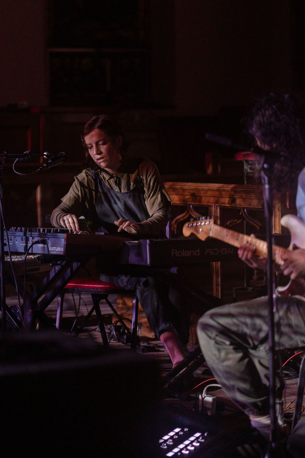 Musicians perform in a dimly lit venue with stage lighting and musical equipment.