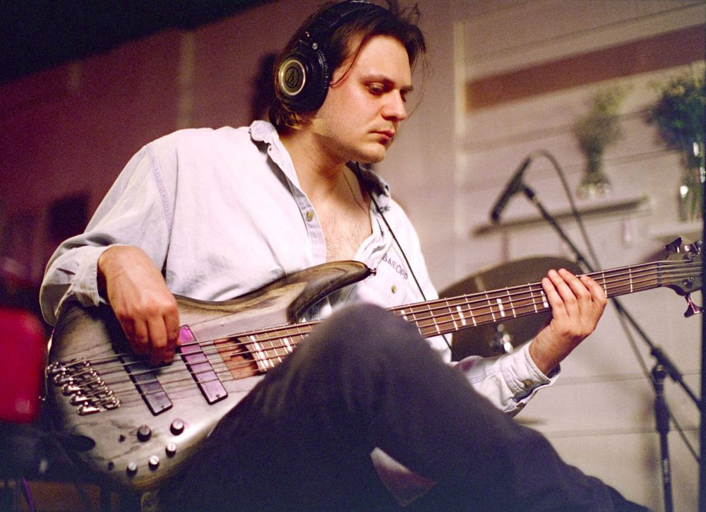 Bass guitarist in headphones playing a silver electric bass guitar during a performance.
