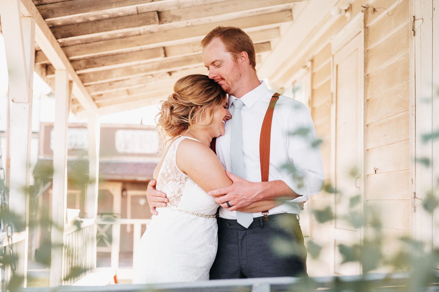 A white couple embraces on their wedding day. The Bride is laughing while the Groom sweetly smells her hair.