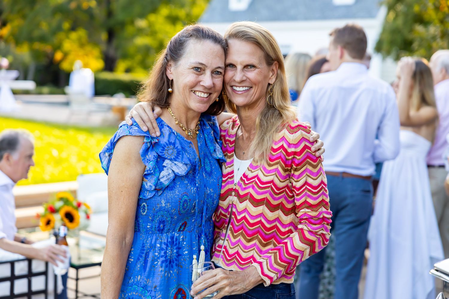 Two women in colorful summer dresses smiling together at outdoor event.