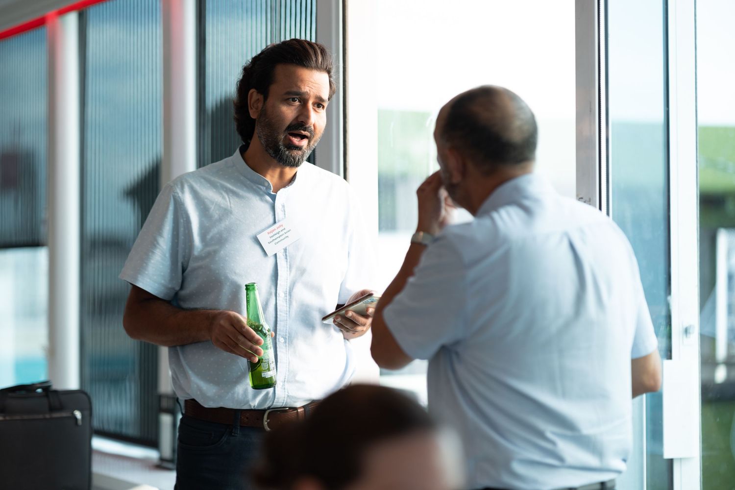 Two businessmen in conversation with drinks at a corporate networking event by window light, business event photography