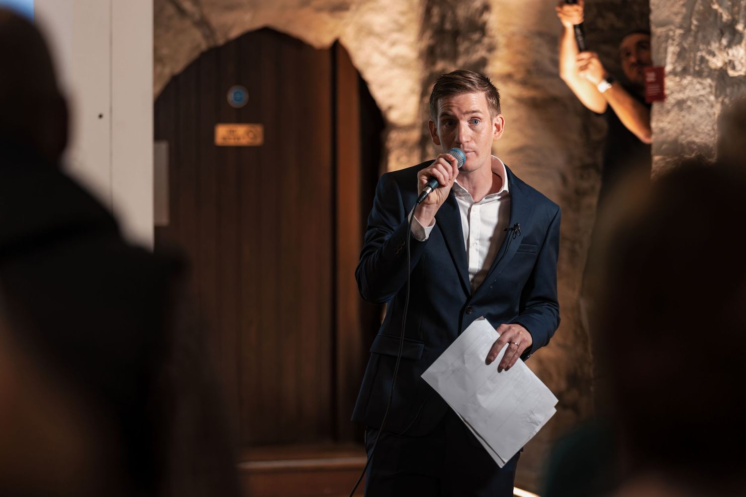 Host speaking into microphone at a corporate event in a stone archway venue, corporate event speaker photography