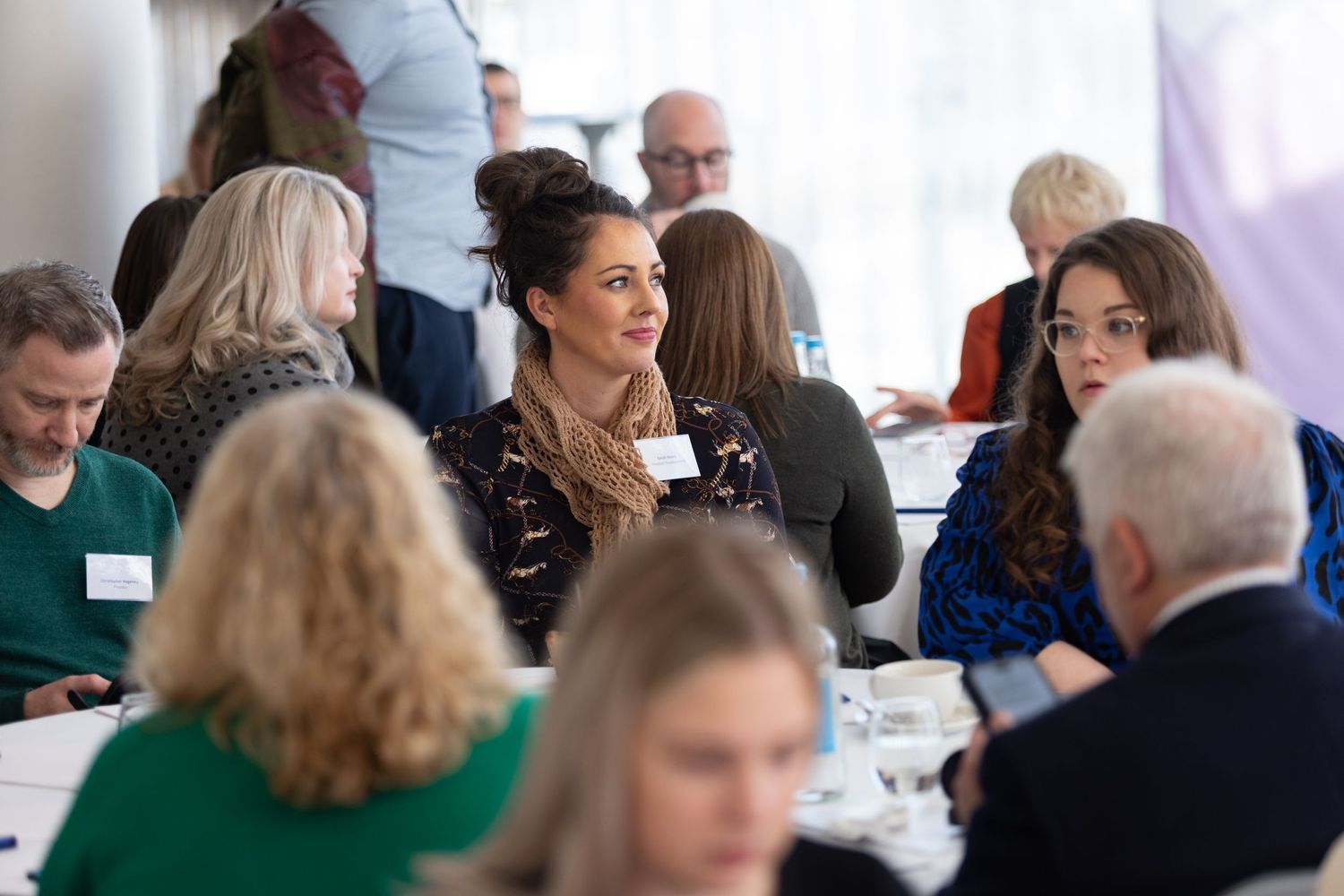 Attendees networking and conversing at tables during a busy corporate conference event, business event photography