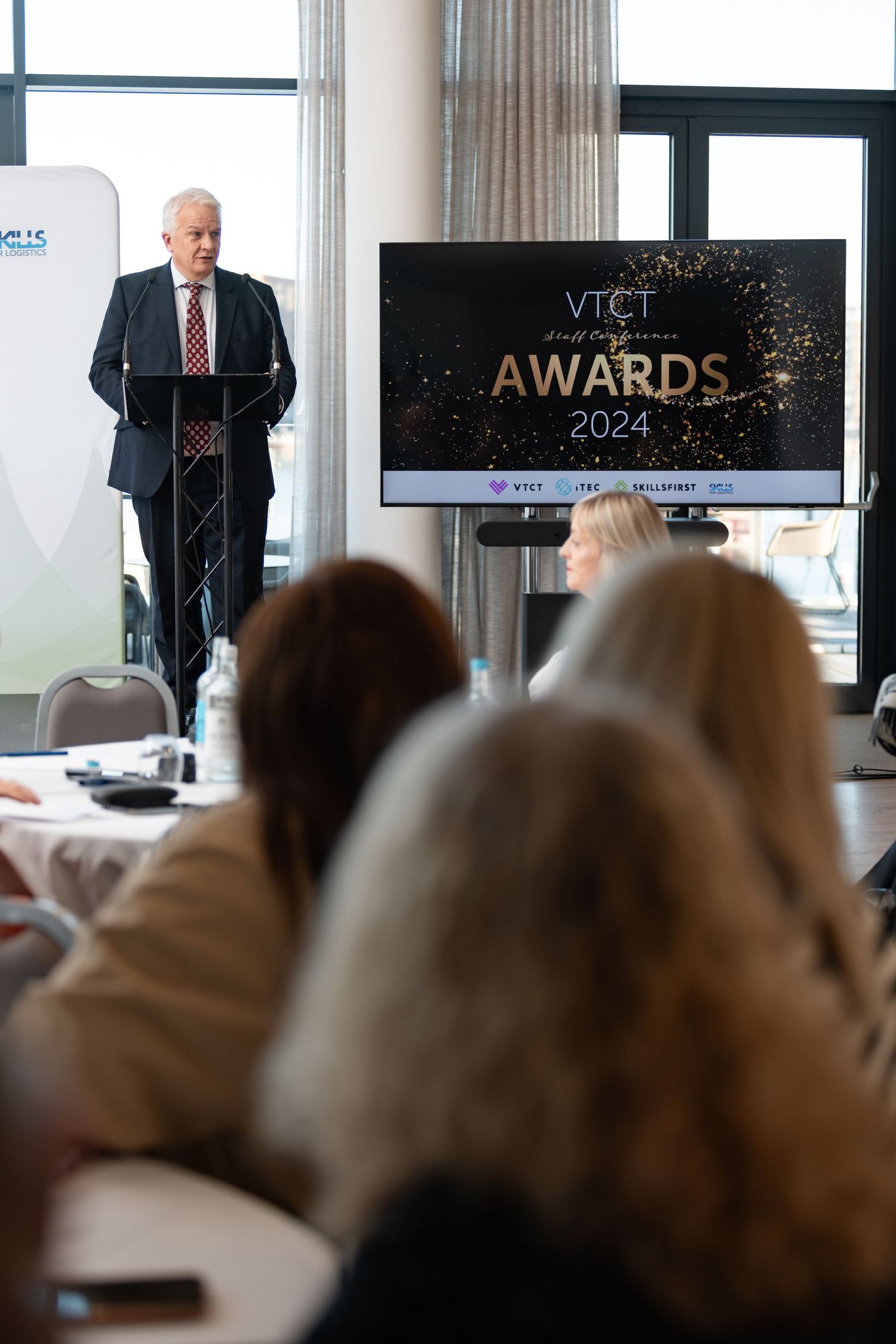 Speaker at podium presenting at the VTCT Awards 2024 ceremony with audience, corporate awards event photography