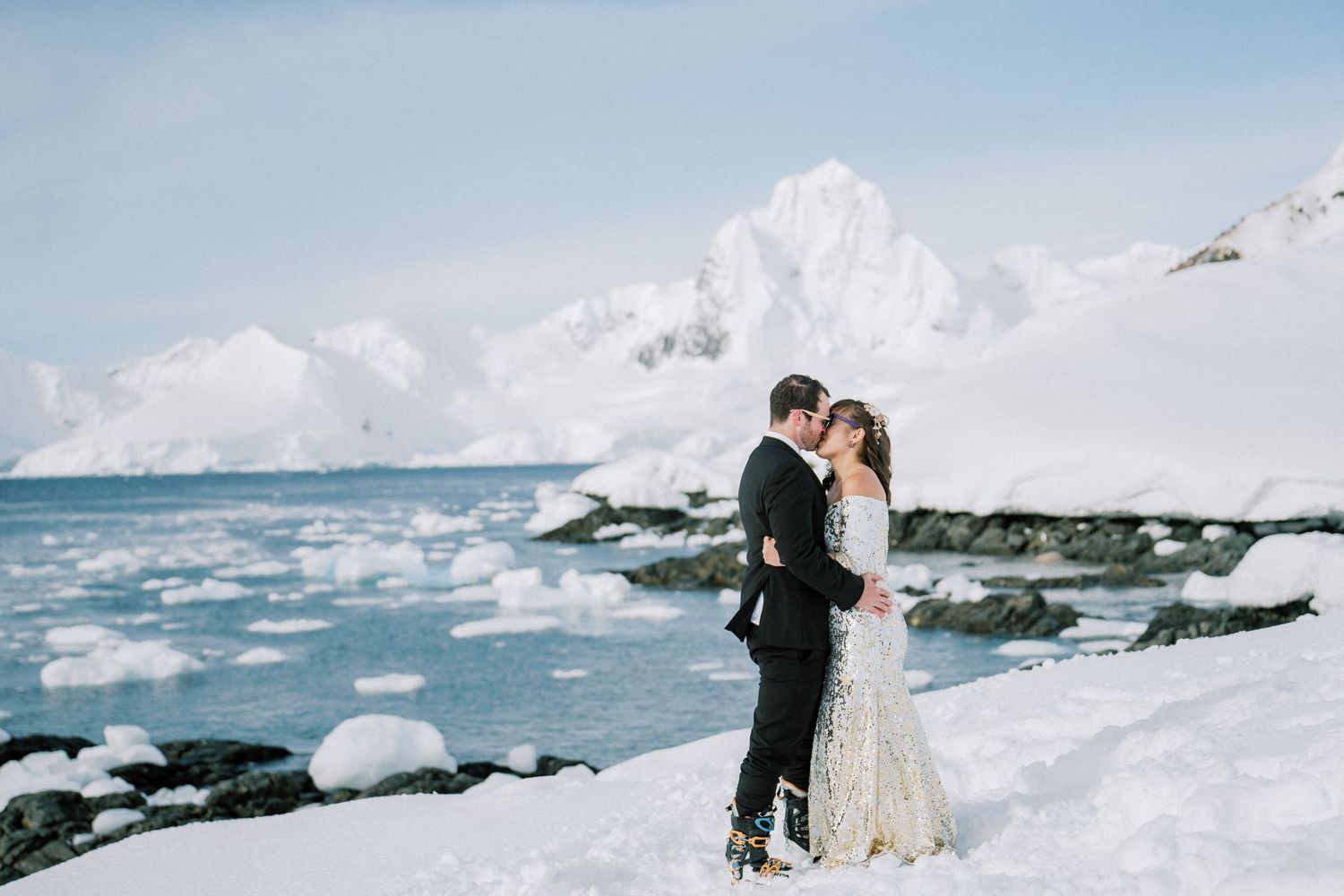 Intimate wedding moment on snowy Antarctic coast with dramatic mountain backdrop.