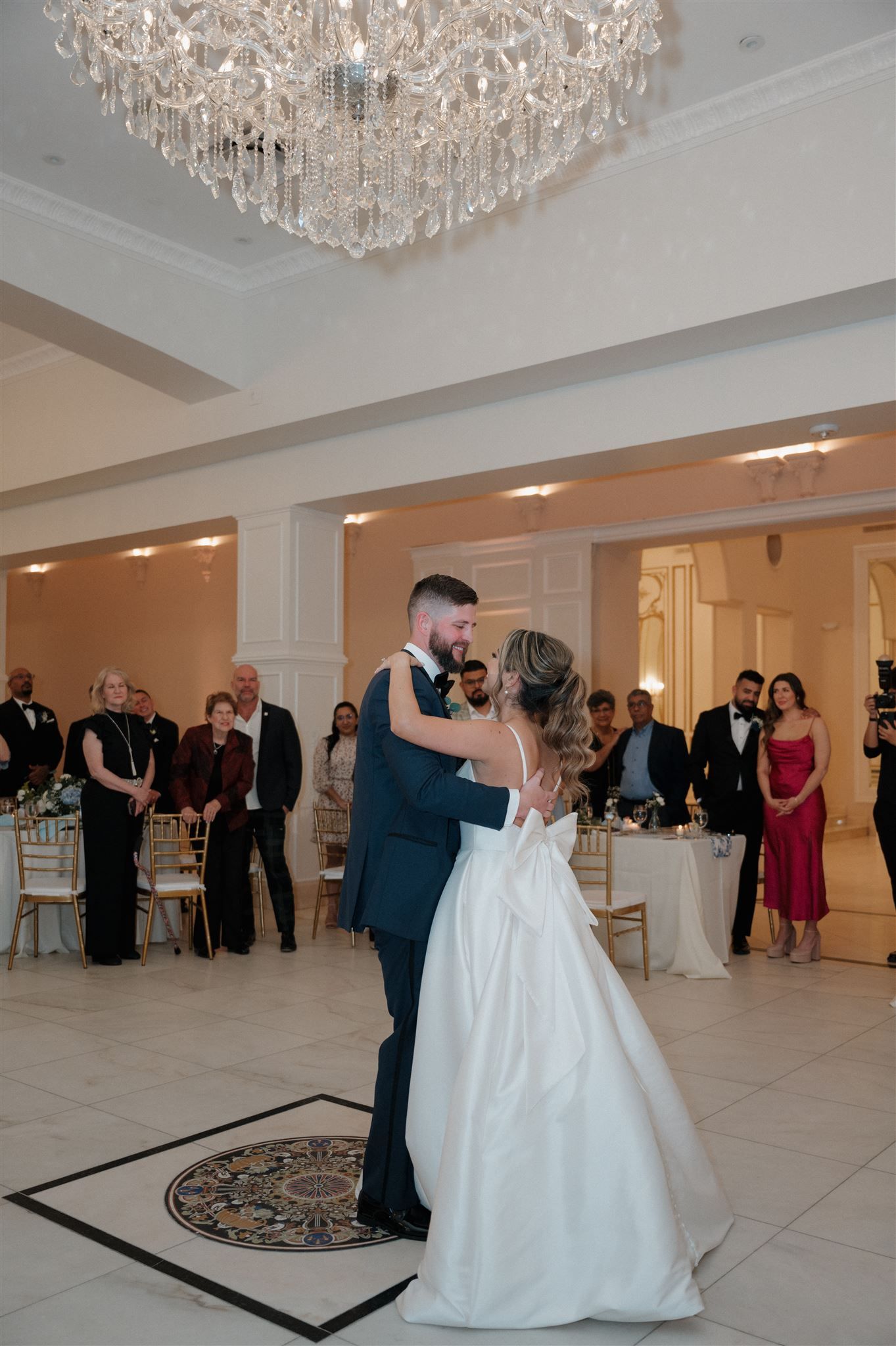 Newlyweds share their first dance under an elegant crystal chandelier in a grand ballroom.