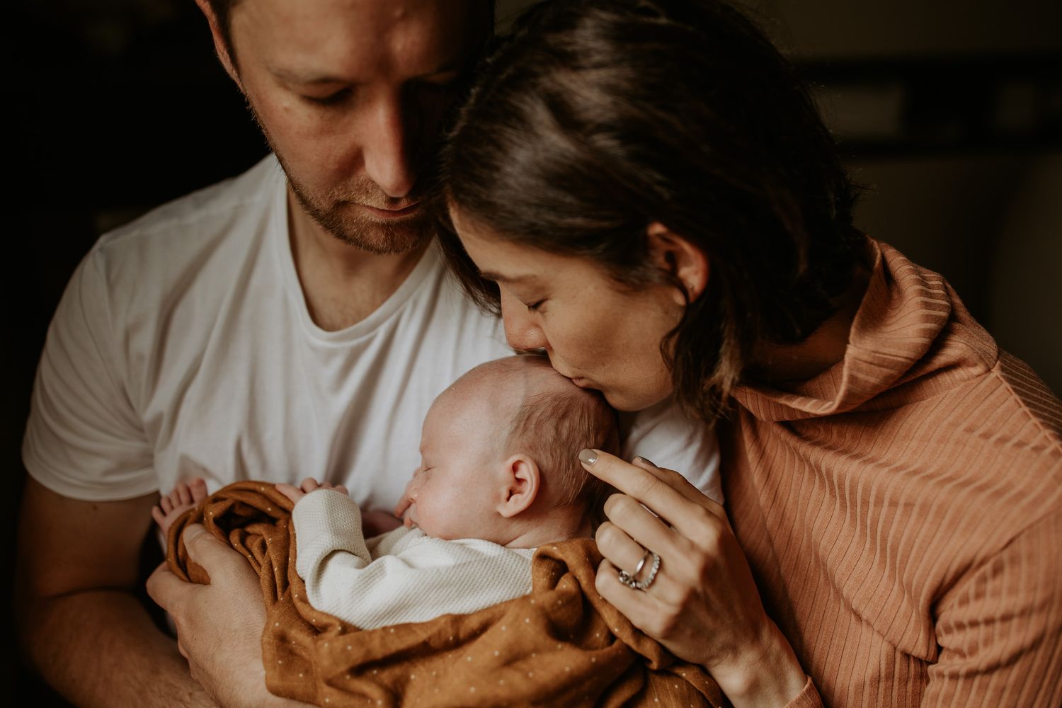 Tender moment captured in warm, moody lighting with an orange blanket.