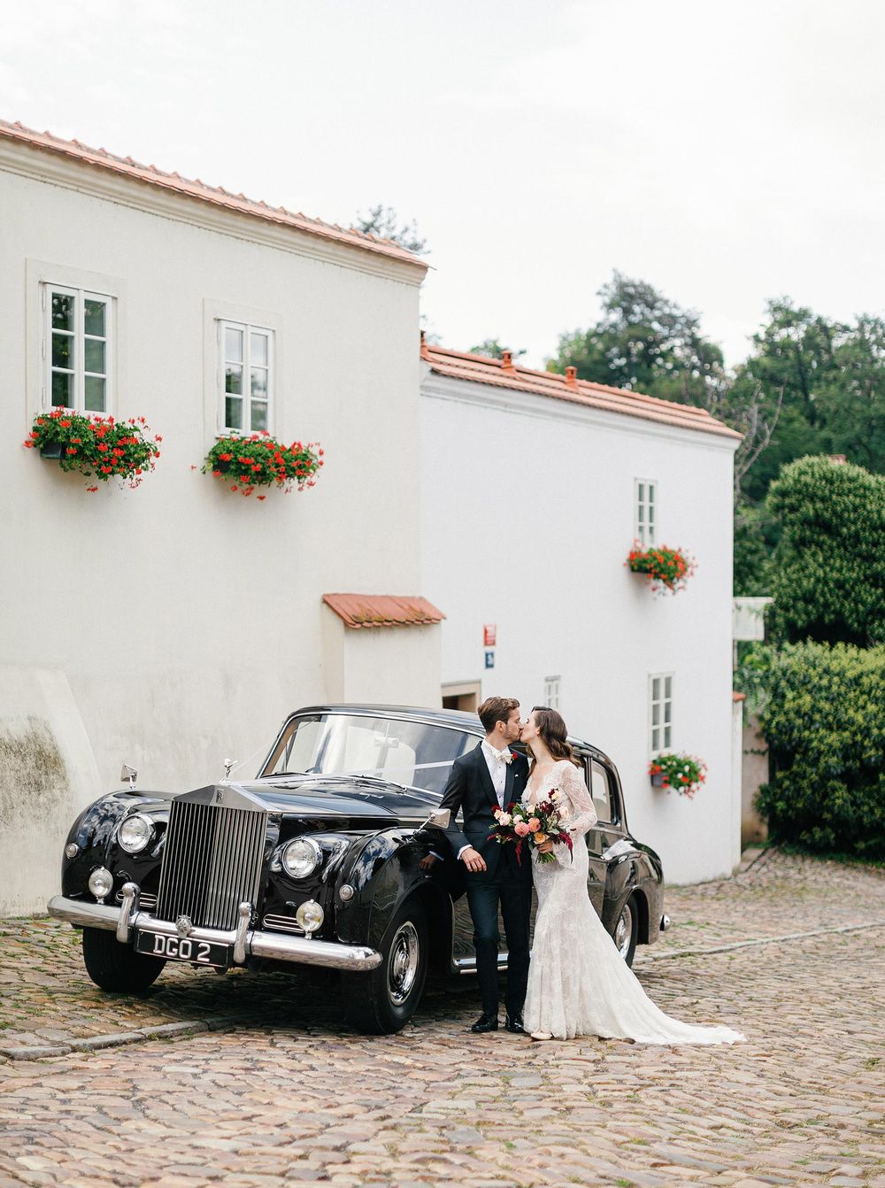 Bride and groom standing next to a Rolls Royce in historic streets of Novy Svet during their Prague wedding.