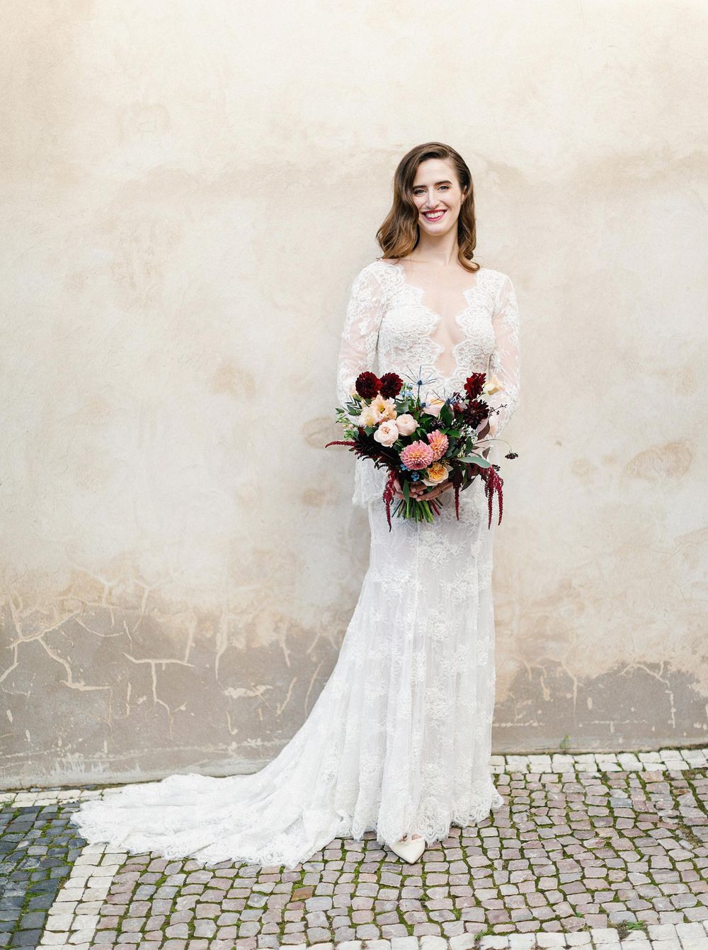 A beautiful bride in a lace wedding dress holding a bouquet, captured in Prague's enchanting atmosphere.