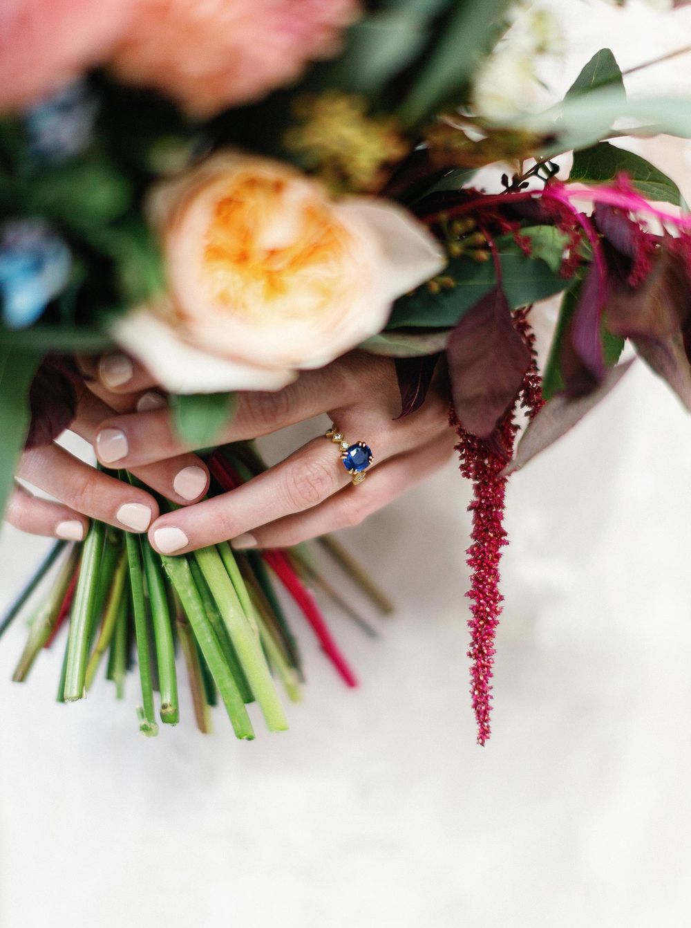 A bride holding her wedding bouquet with a ring, featuring a beautiful blue stone.