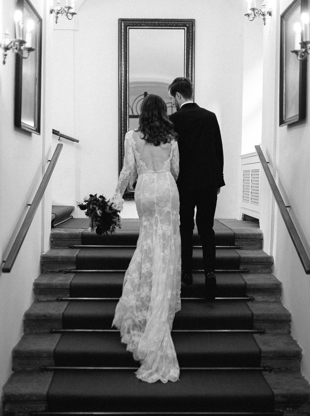 A smiling bride in a white dress and a groom in a black suit stand together.
