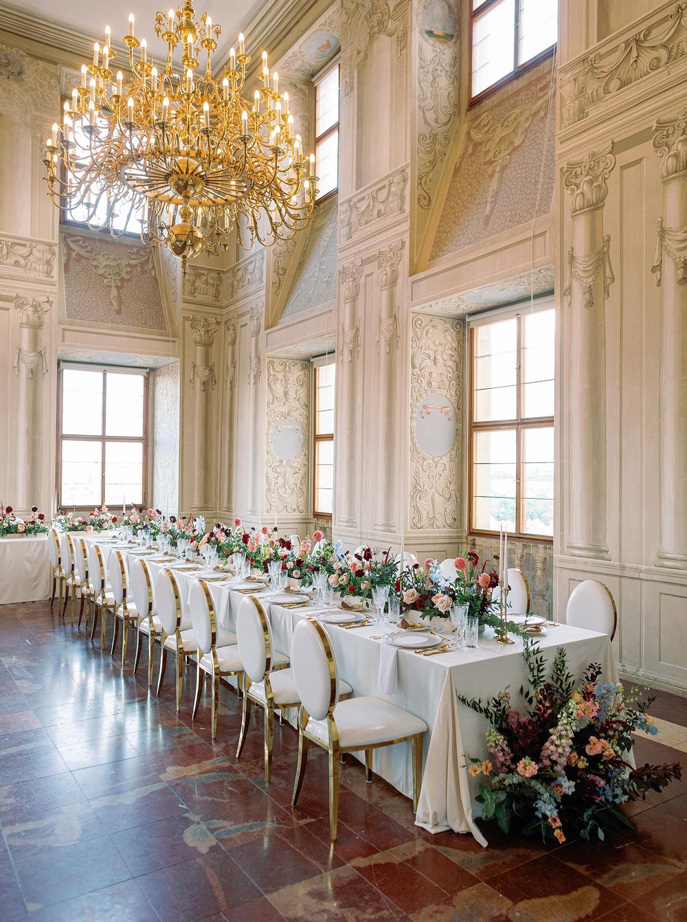 Elegant dining room with chandelier and gold tablecloths at wedding reception table in Lobkowicz Palace, Prague.