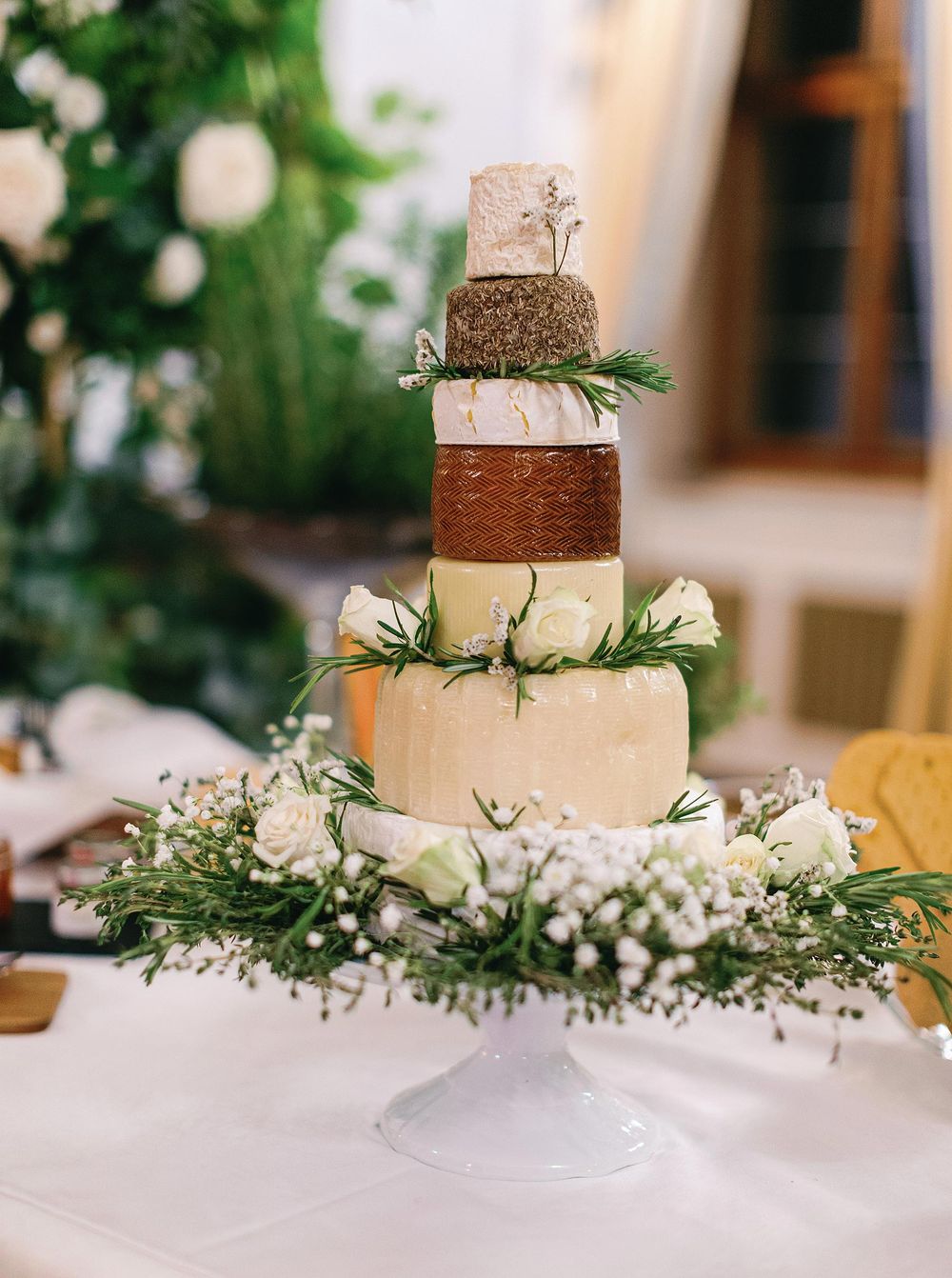 Wedding cake made of cheese, beautifully decorated with intricate designs and garnished with fresh herbs.