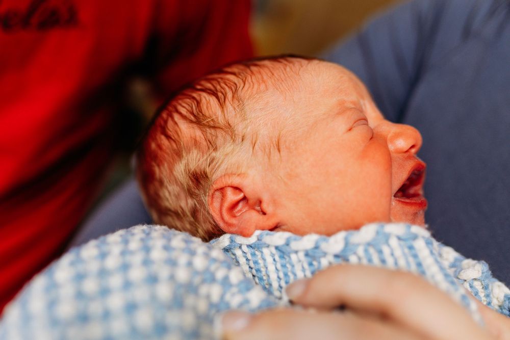 Newborn baby yawning while being cradled in parents arms in hospital room.