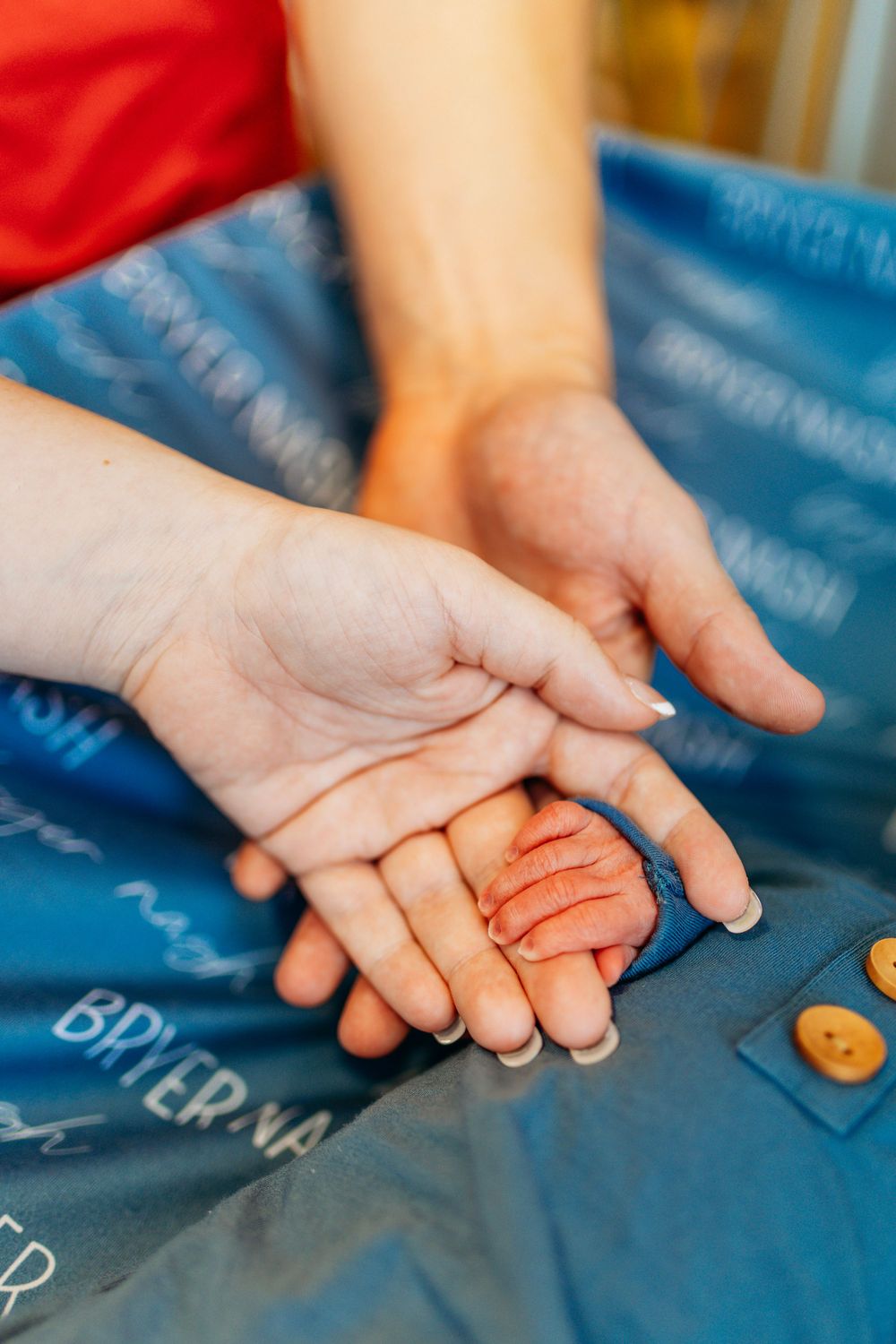 Adult hands gently holding tiny newborn baby feet on blue Bryer Nash blanket.
