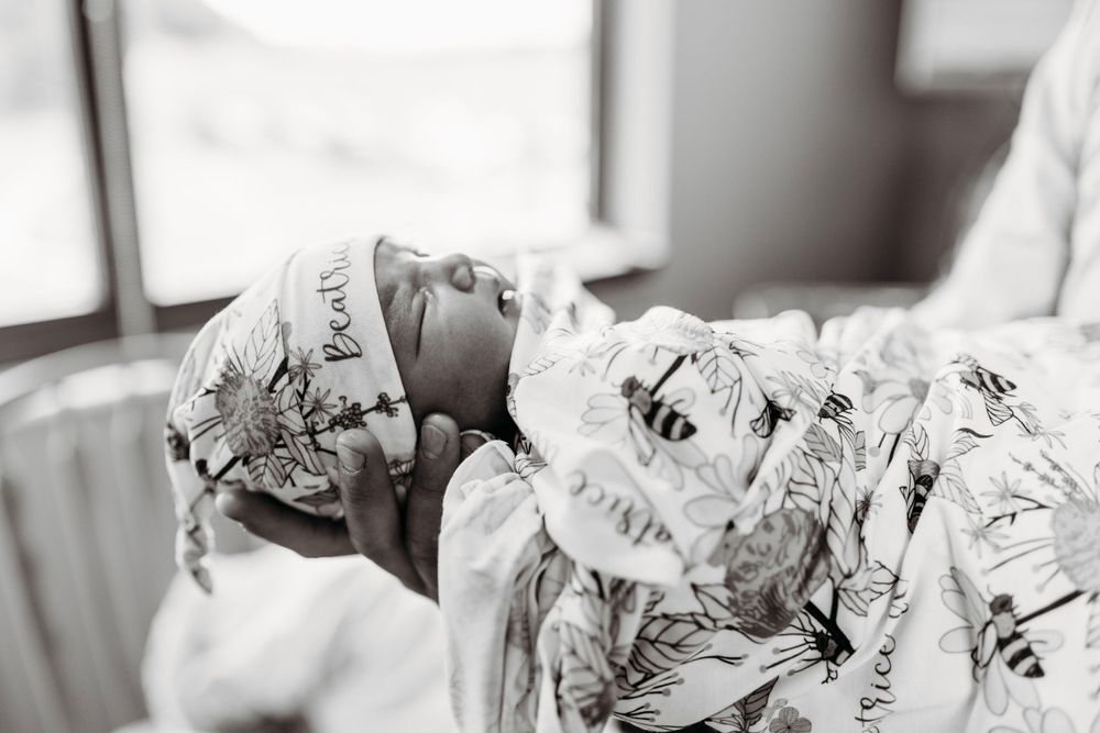 Black and white portrait of peaceful sleeping newborn wrapped in patterned swaddle blanket in hospital bassinet.