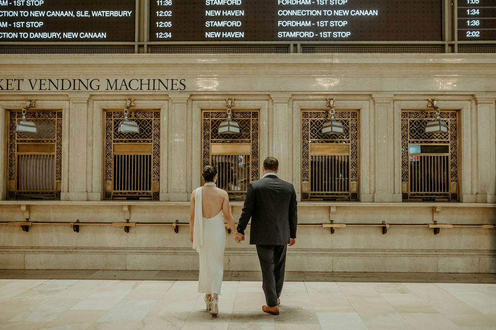 Couple stands holding hands in front of classic ticket vending machines.