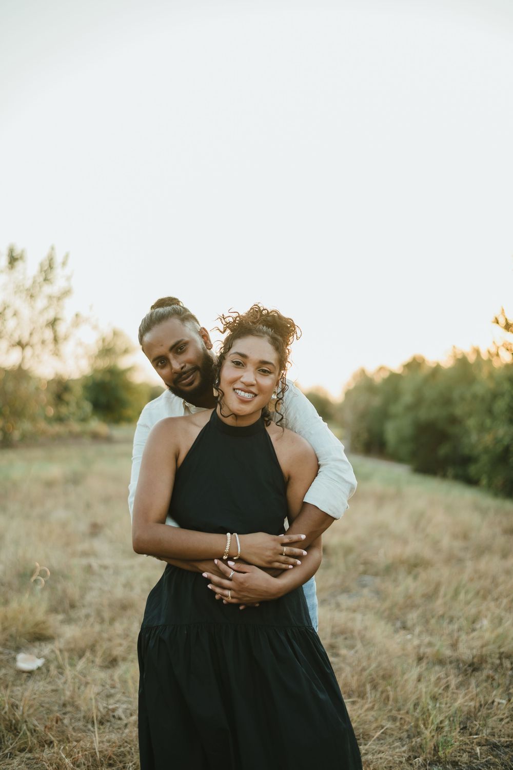 Happy couple embracing in a field during golden hour photography session.