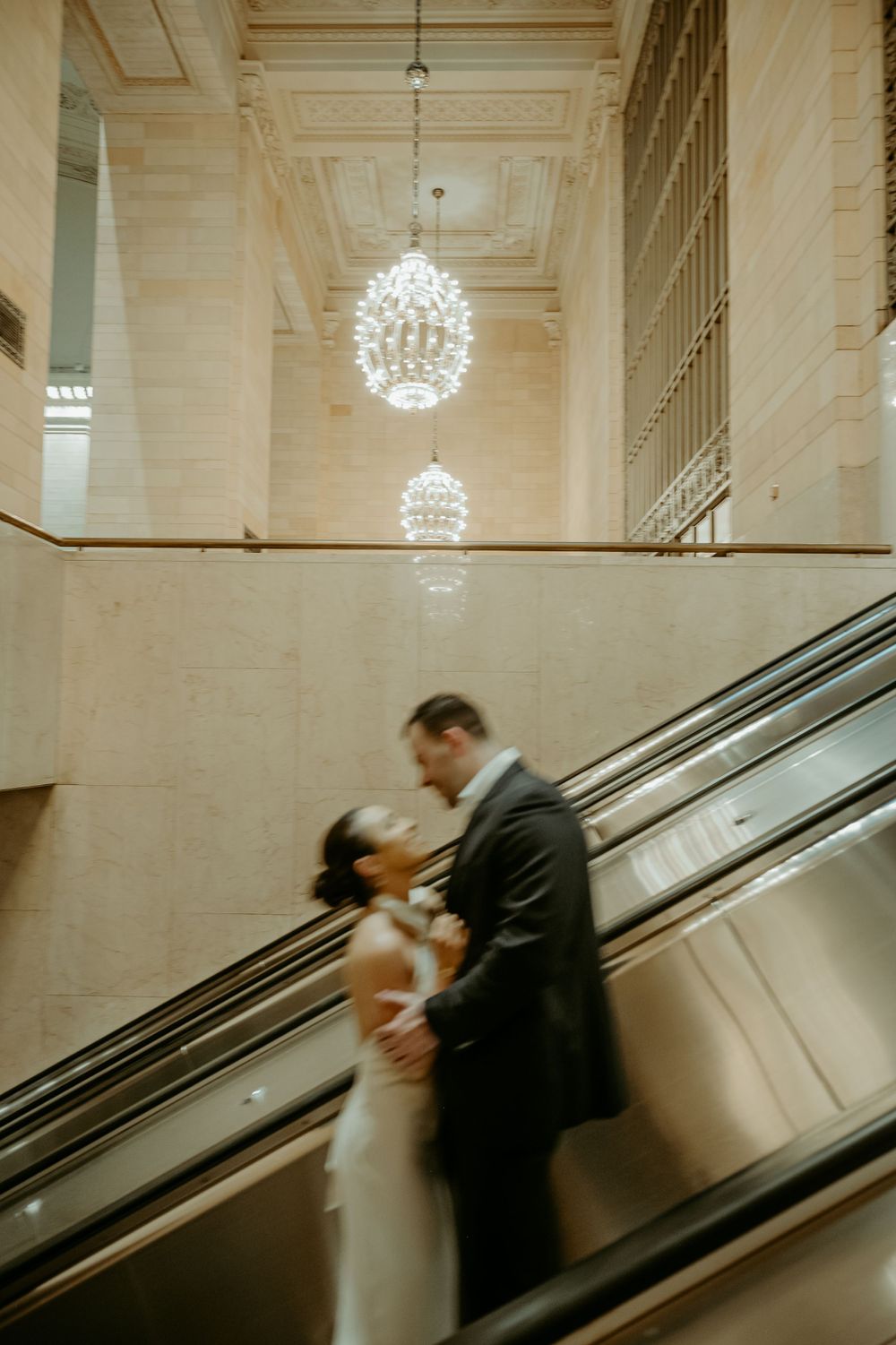 Couple sharing intimate moment on escalator under crystal chandeliers in elegant building.