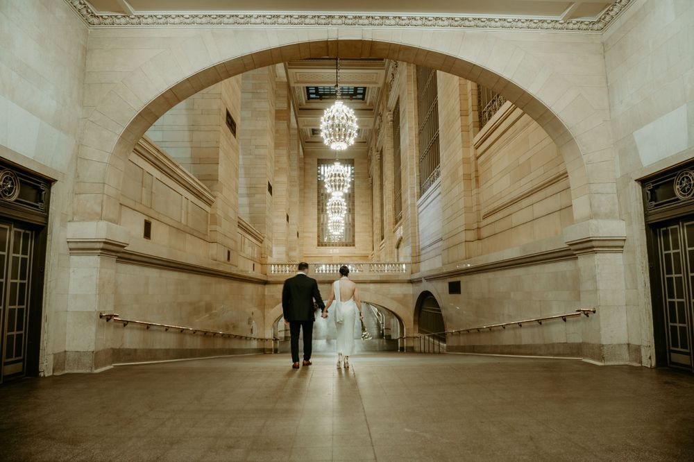 Silhouetted couple walking through grand arched hallway with chandelier.