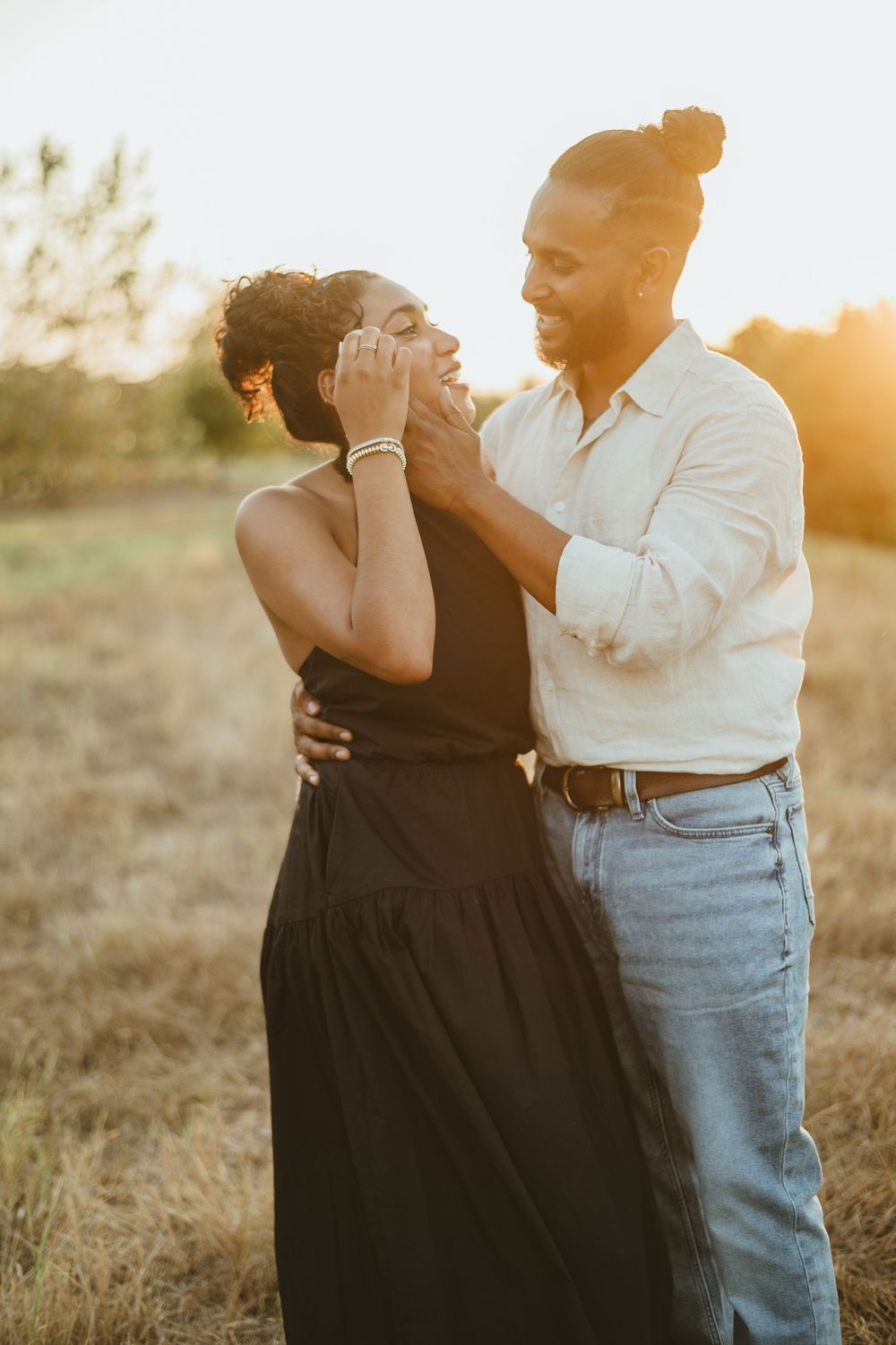 Couple sharing a playful and romantic moment in a field at sunset.