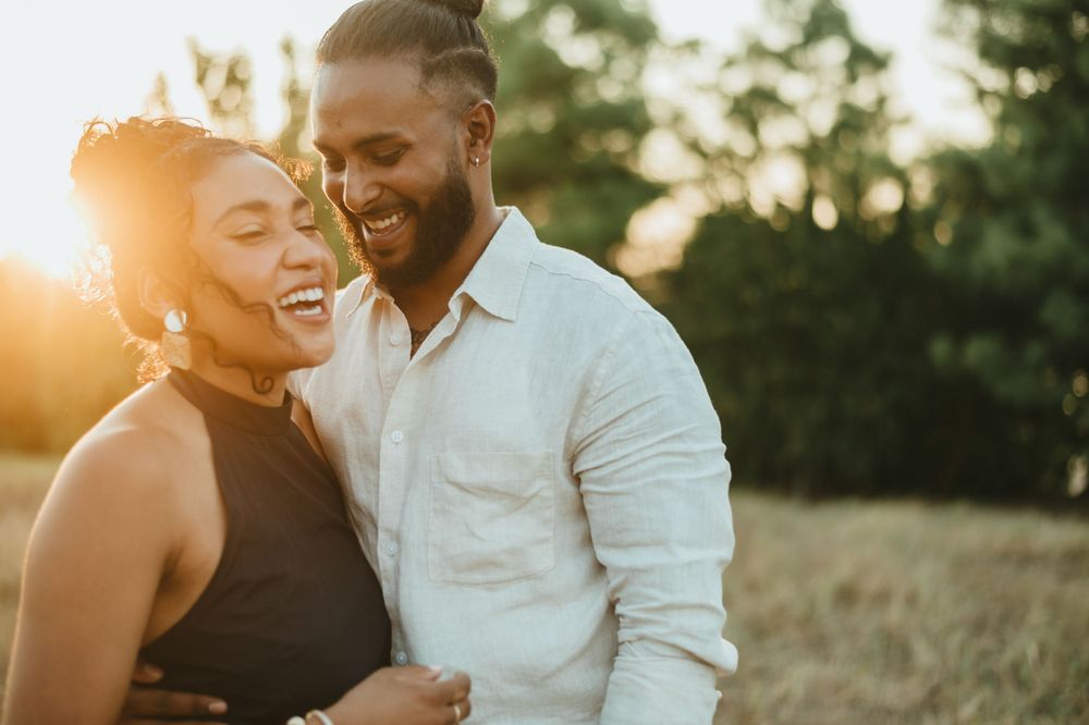 Couple laughing together during sunset photoshoot in natural setting.