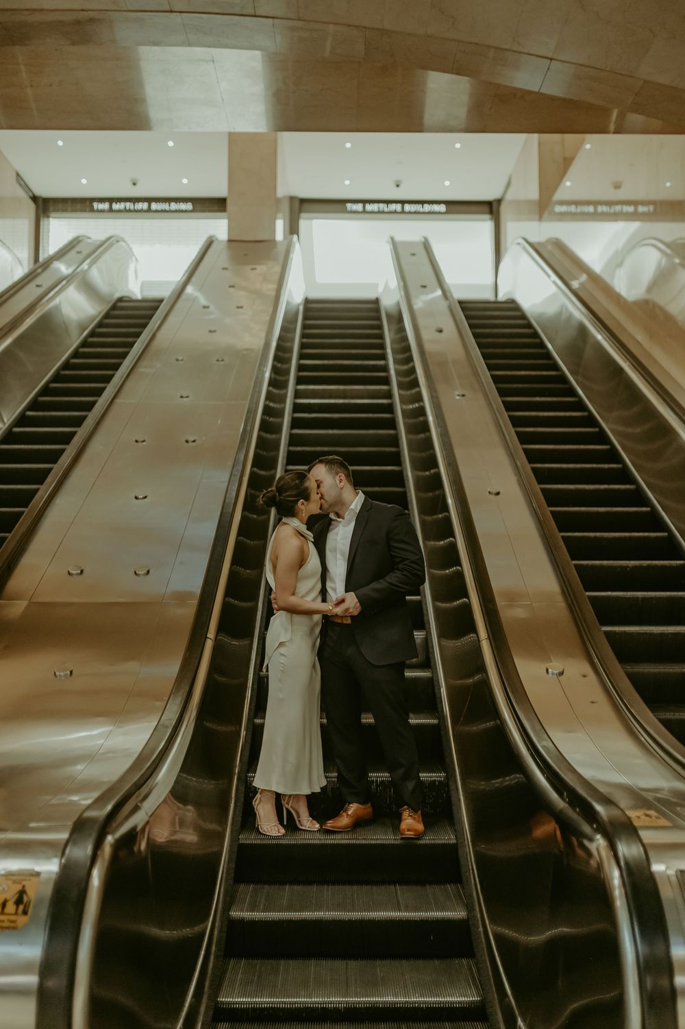 A couple shares an intimate moment on subway escalators in a moody, atmospheric setting.