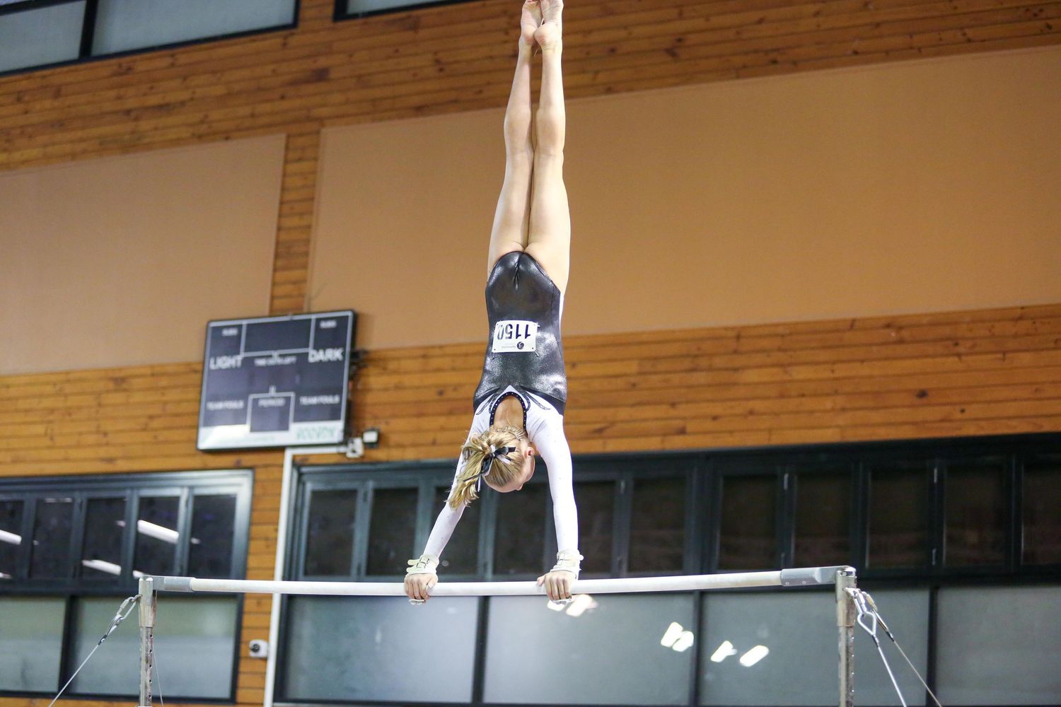 Athletic performance on high bar showing inverted handstand position in gymnastics competition.