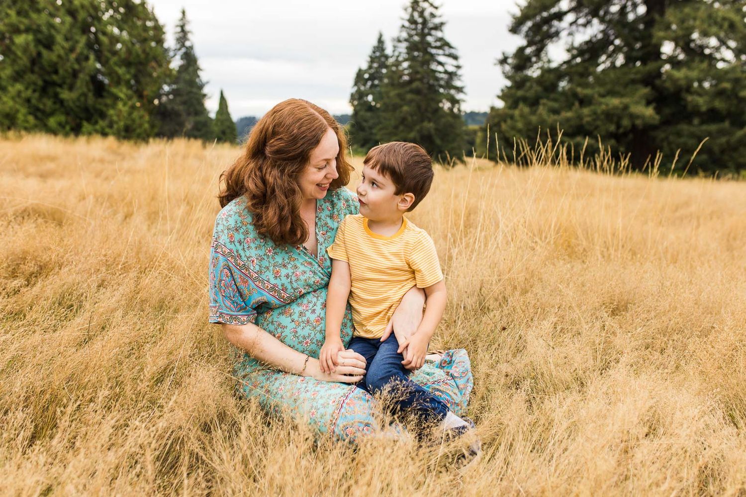 Son sitting in mom's lap, sharing a tender moment together, in a grassy field in Woodinville