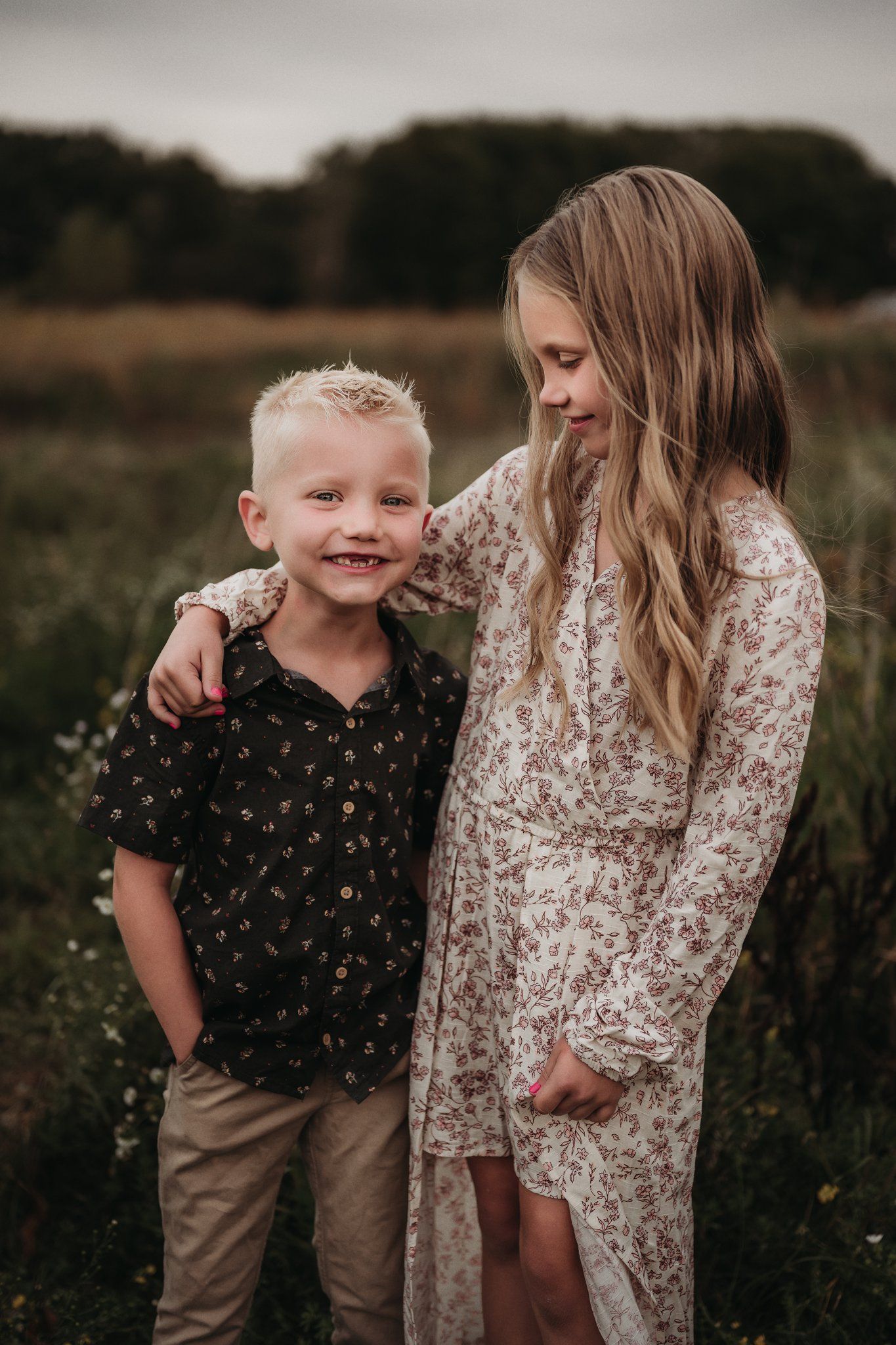 Two figures embrace in a wildflower field at sunset wearing floral patterned clothing.
