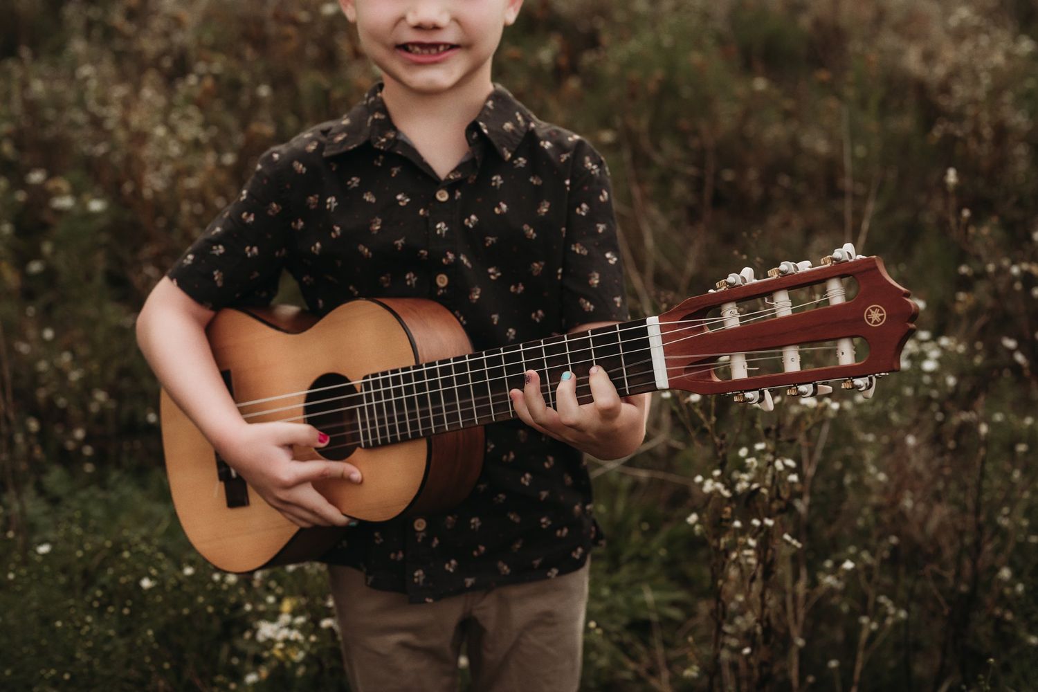 Close-up shot of hands strumming acoustic guitar strings in meadow.