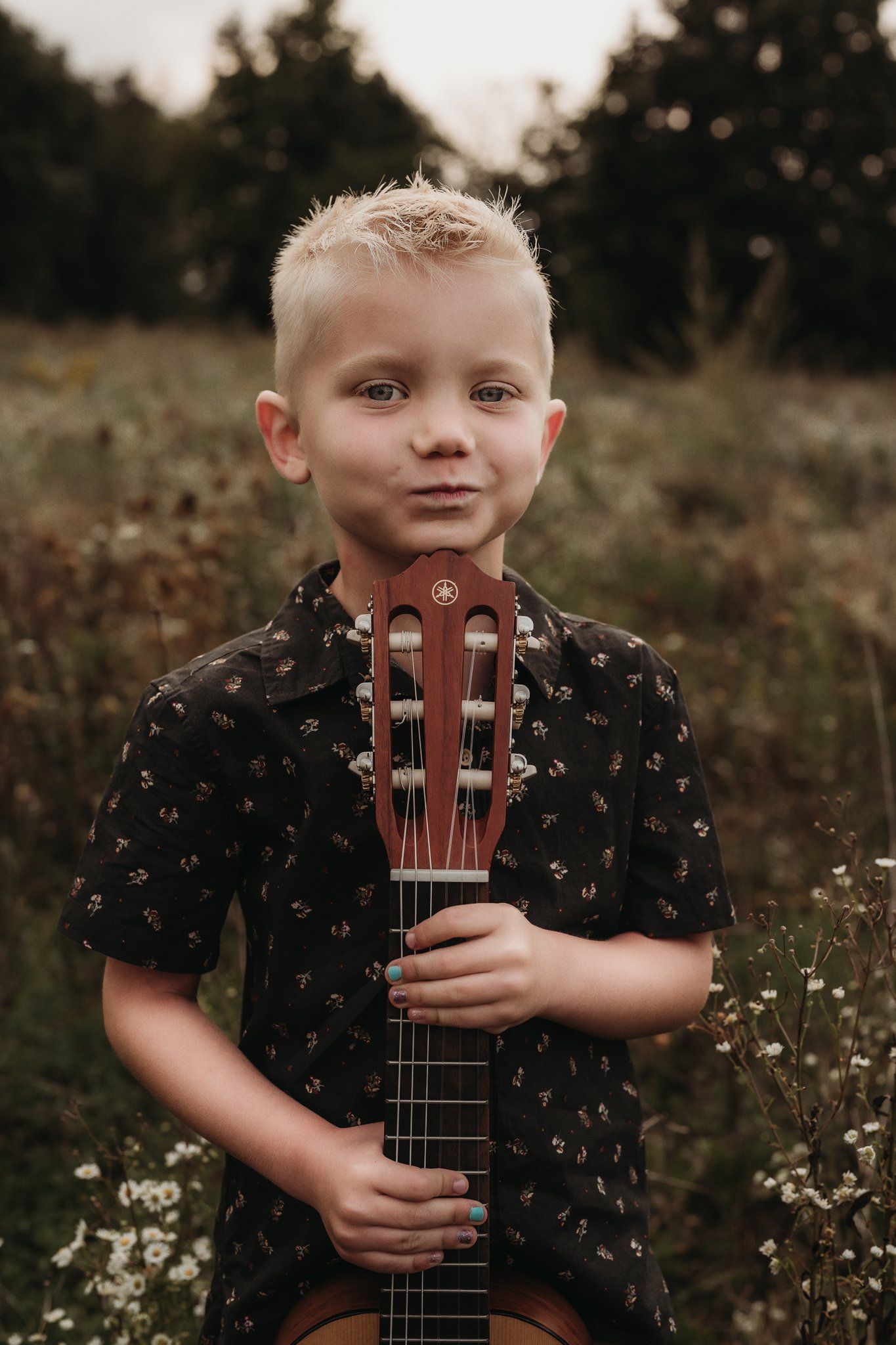 Portrait of young guitarist holding acoustic guitar in flower-filled field.