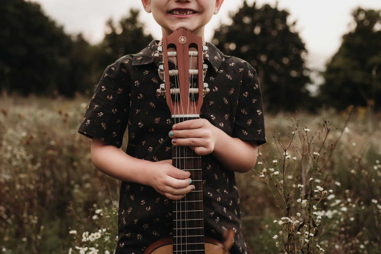 Close-up view of hands holding guitar neck against floral background.