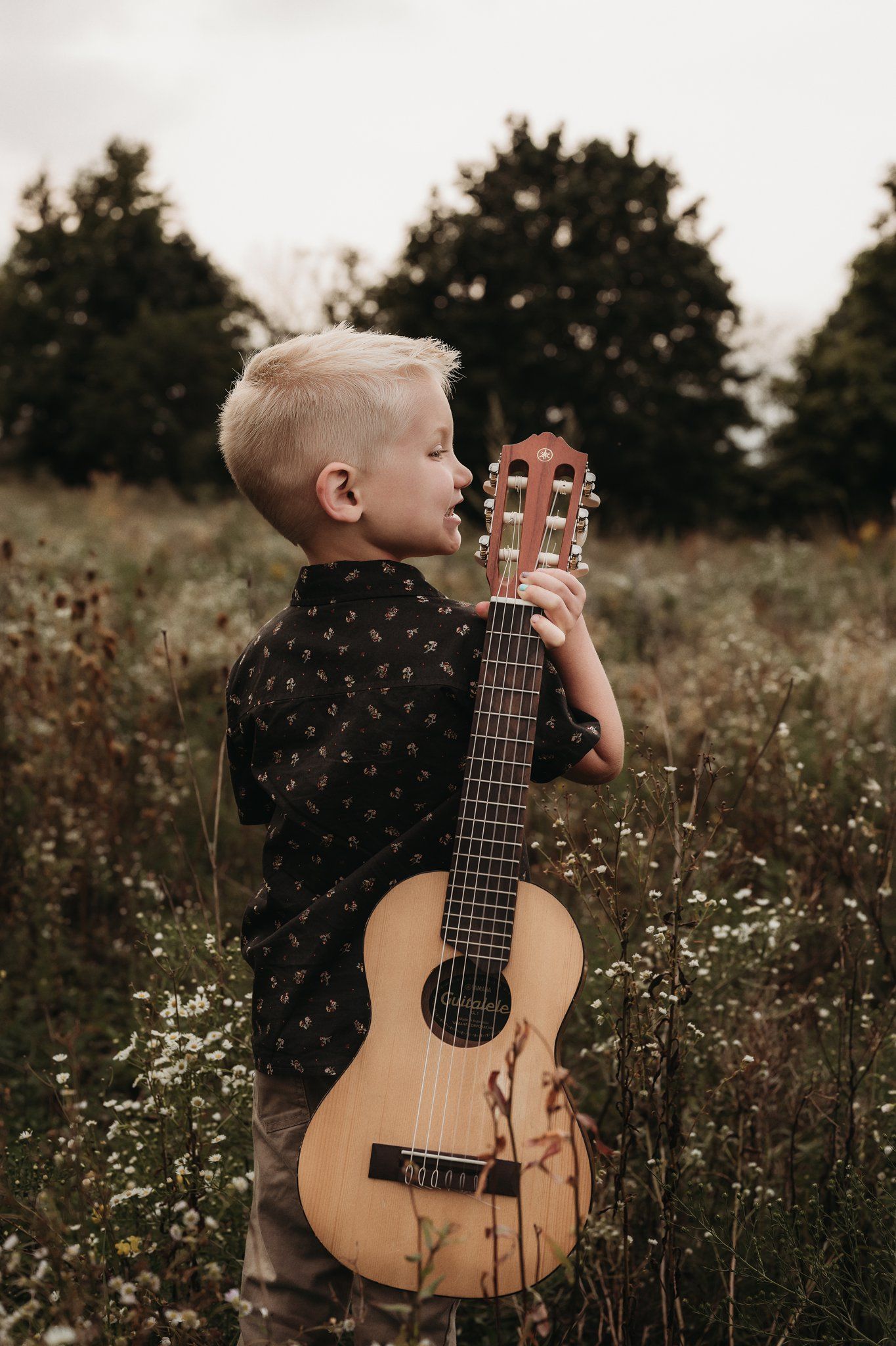 Side view of young guitarist holding acoustic instrument in natural setting.