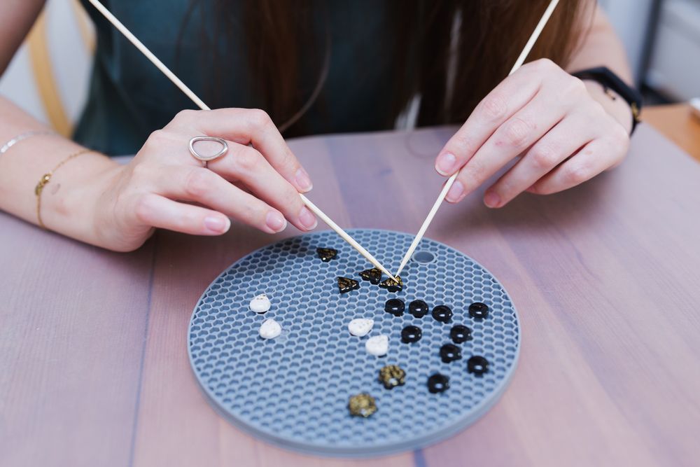 Hands arranging black and white beads on circular blue pegboard pattern.