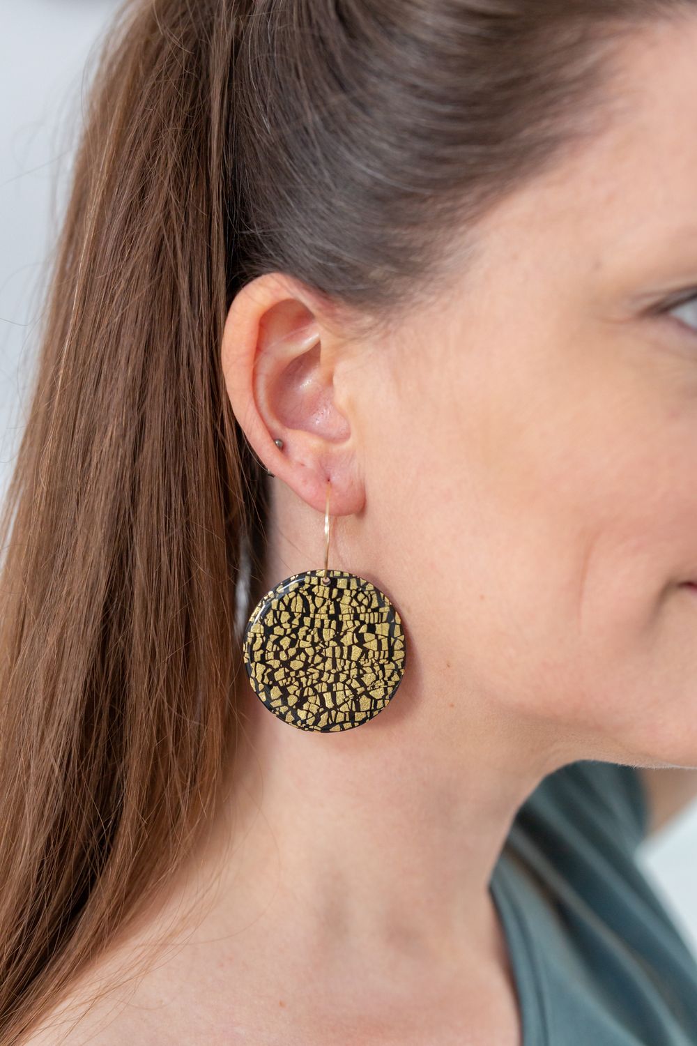 Close-up of a textured gold circular earring against natural lighting.