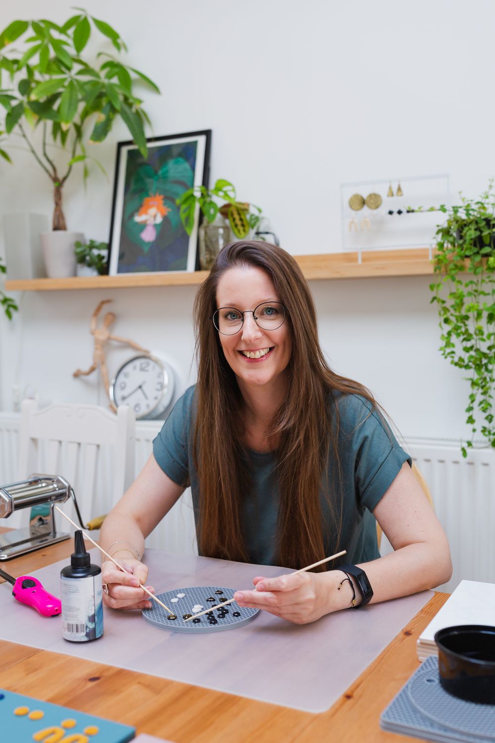 Artist working at a desk surrounded by plants and creative materials.