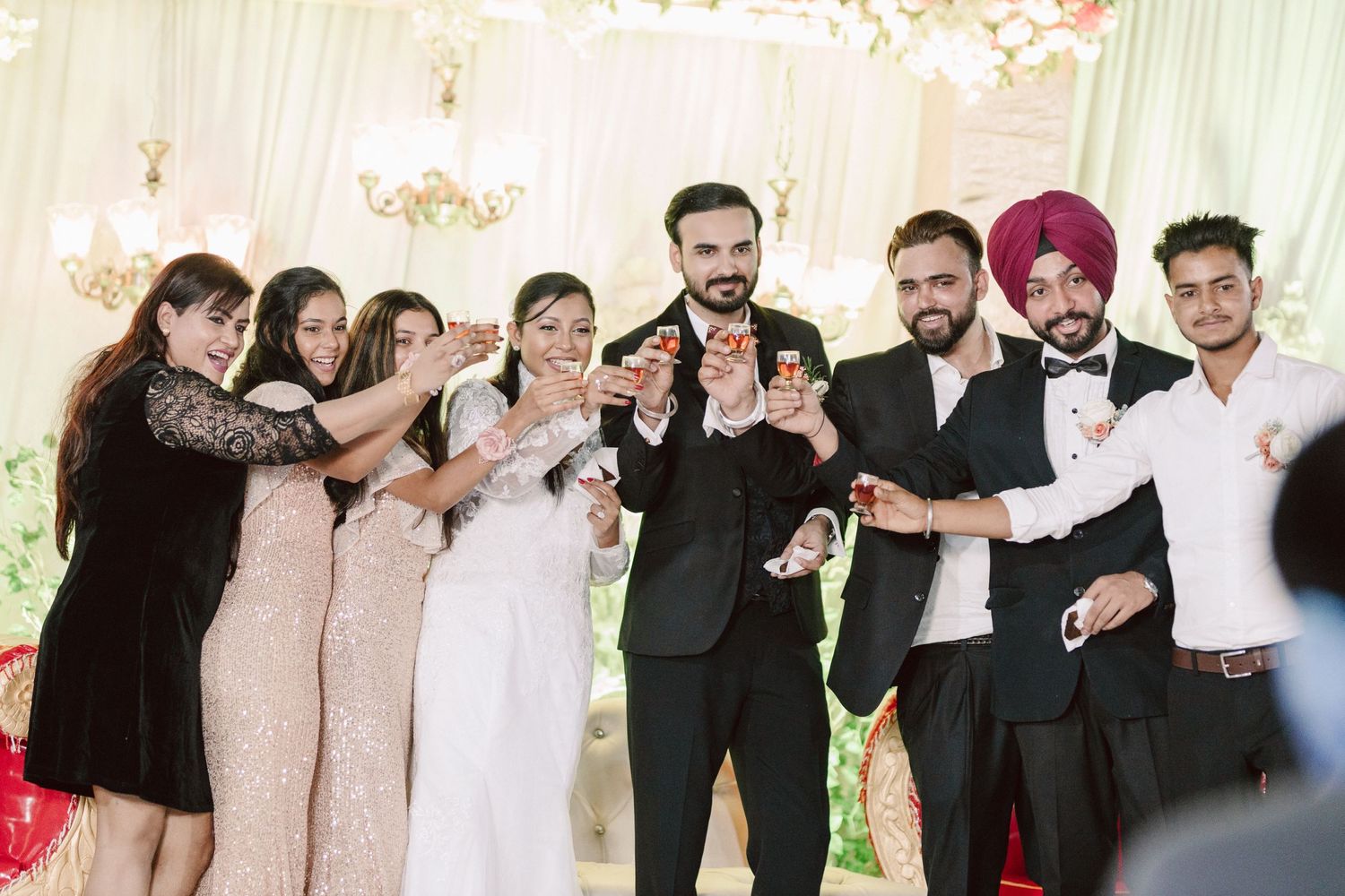 Wedding party members lined up in formal attire against a floral backdrop.
